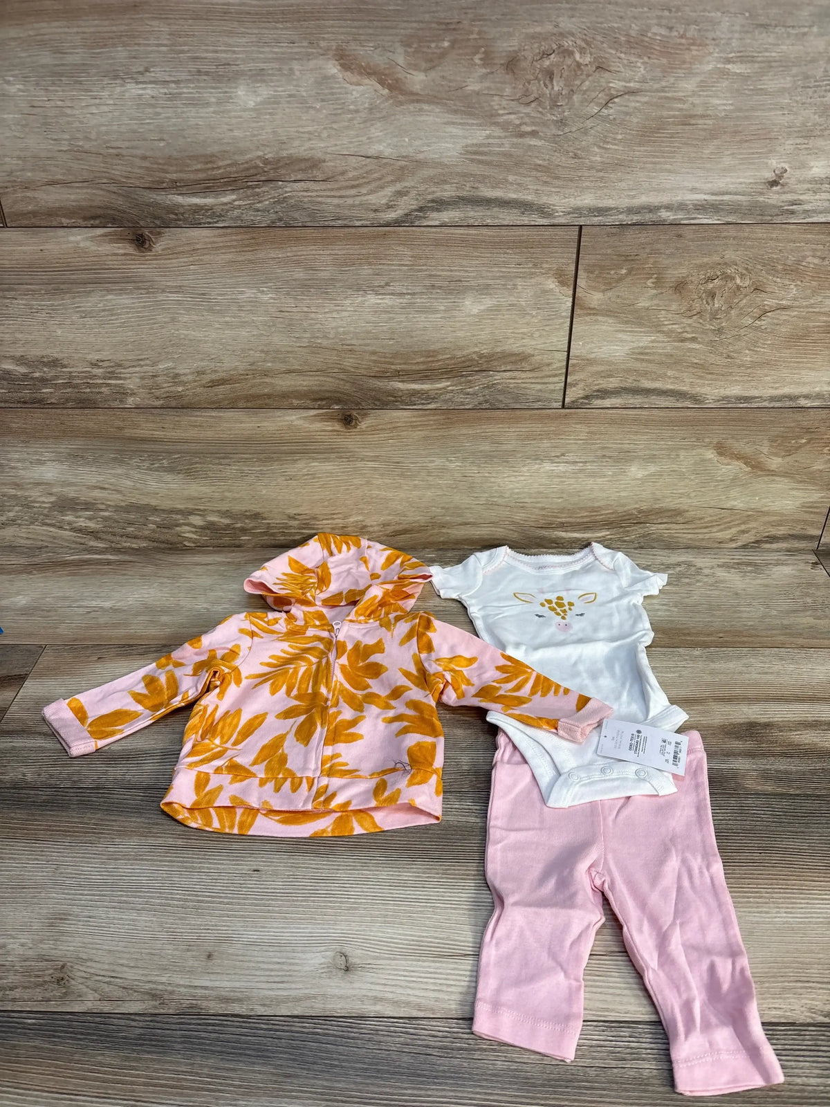 Pink baby outfit set with floral hoodie, white giraffe bodysuit, and pink pants on wood floor