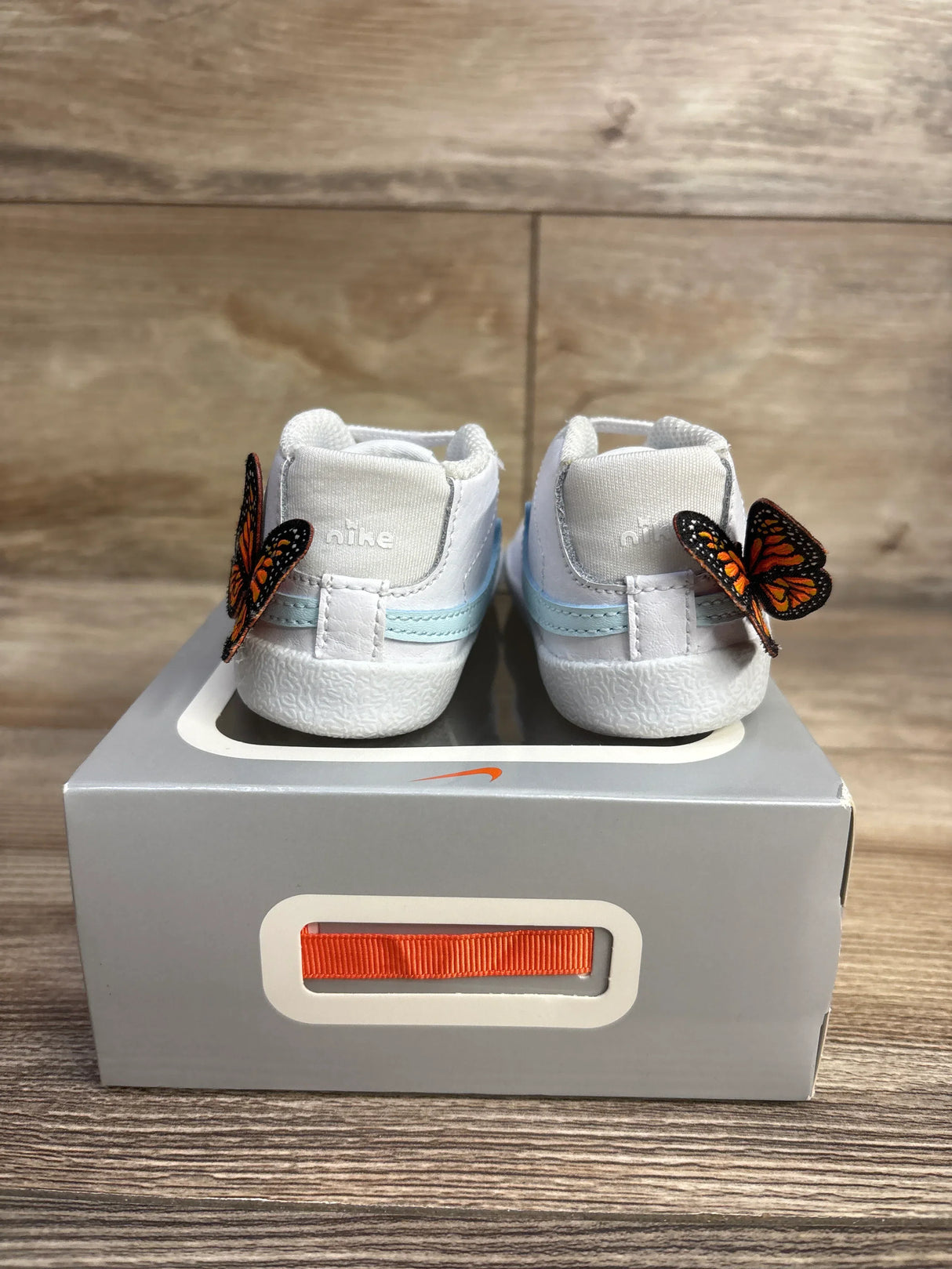 Pair of white toddler Nike shoes with light blue accents and butterfly decorations, displayed on a gray Nike box