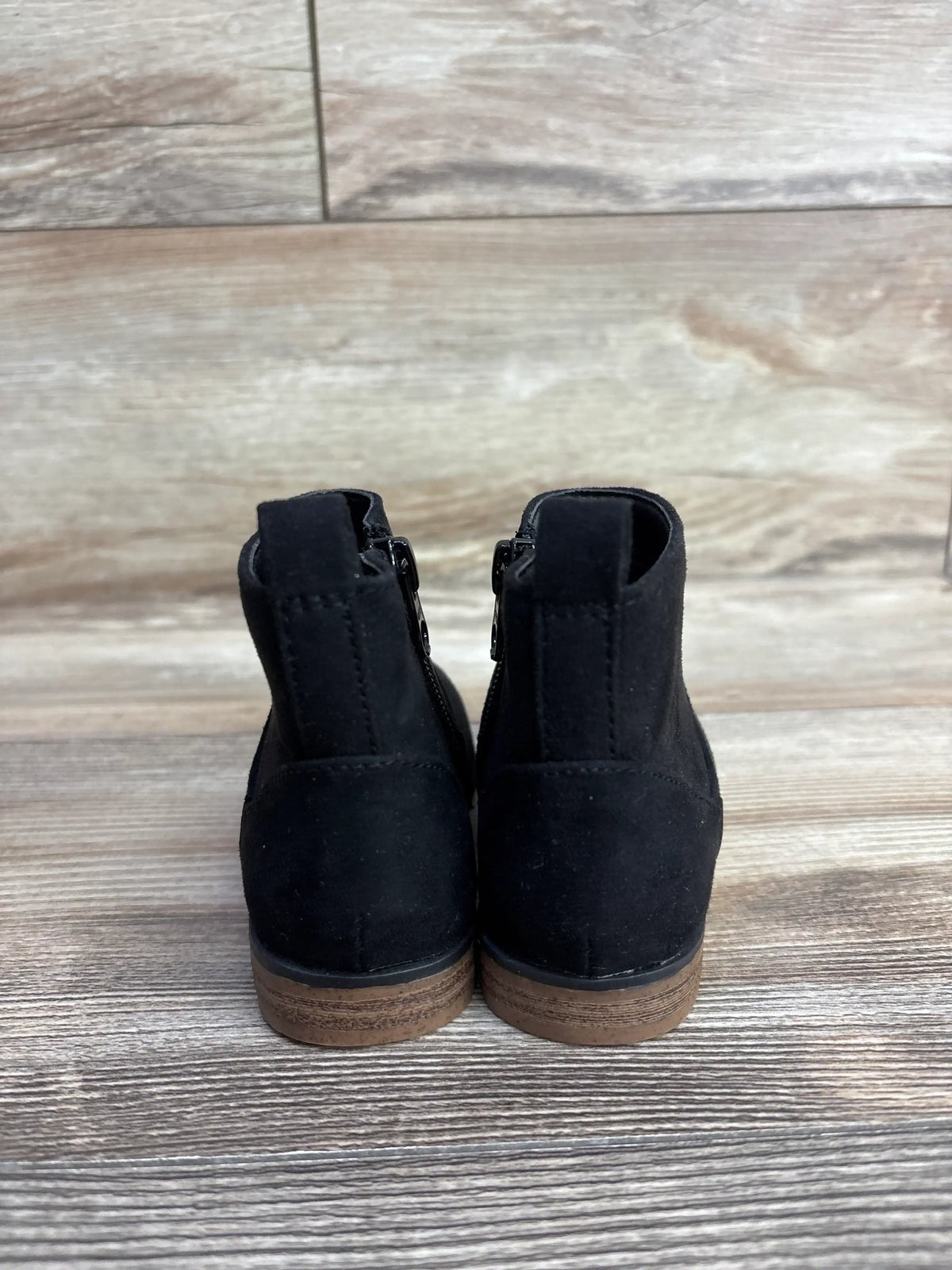 Black suede children's ankle boots with brown soles, rear view on wooden floor