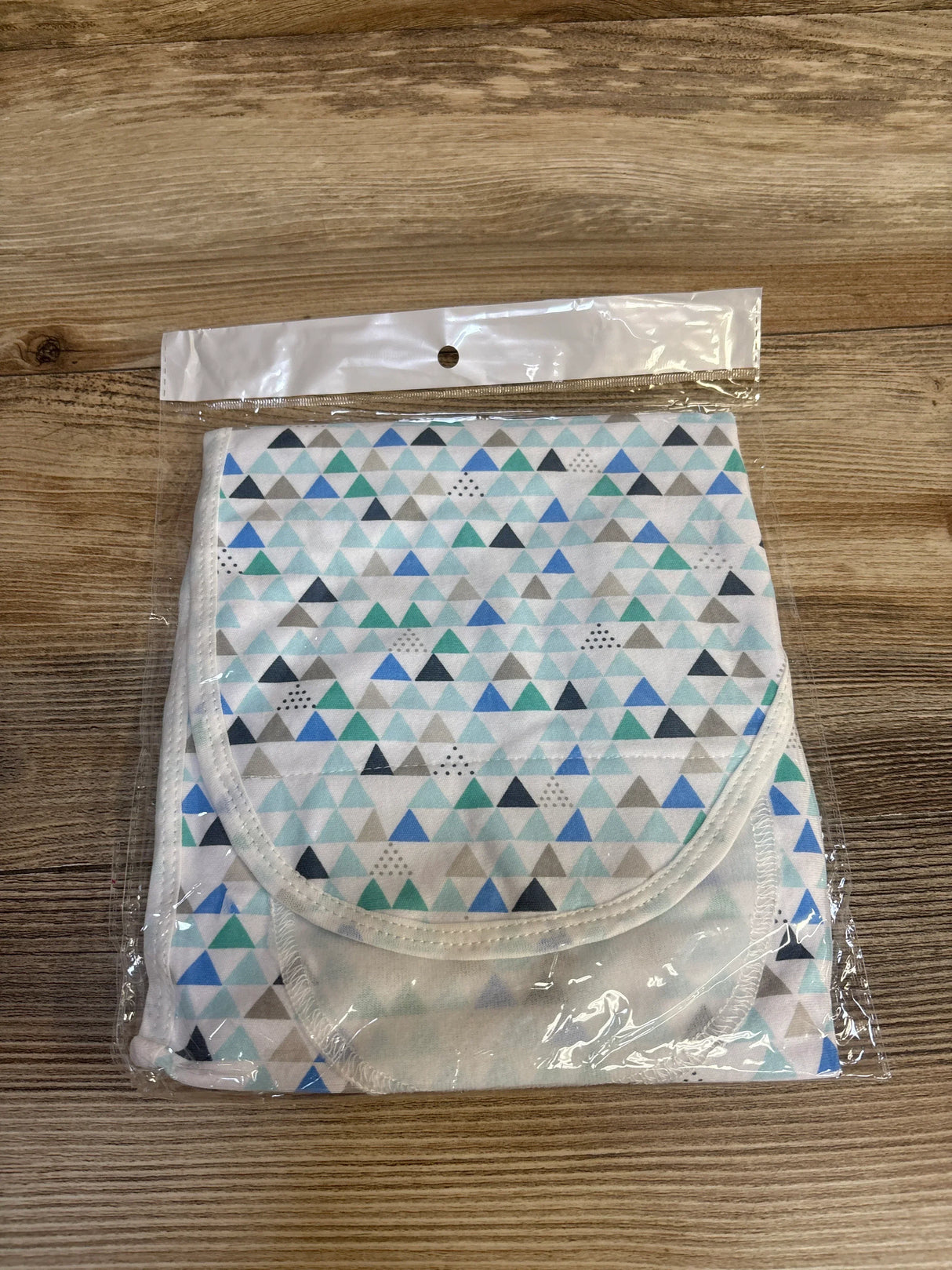 Front view of packaged Ramede newborn swaddle wrap with matching hat showcasing blue and green triangle pattern on wooden surface