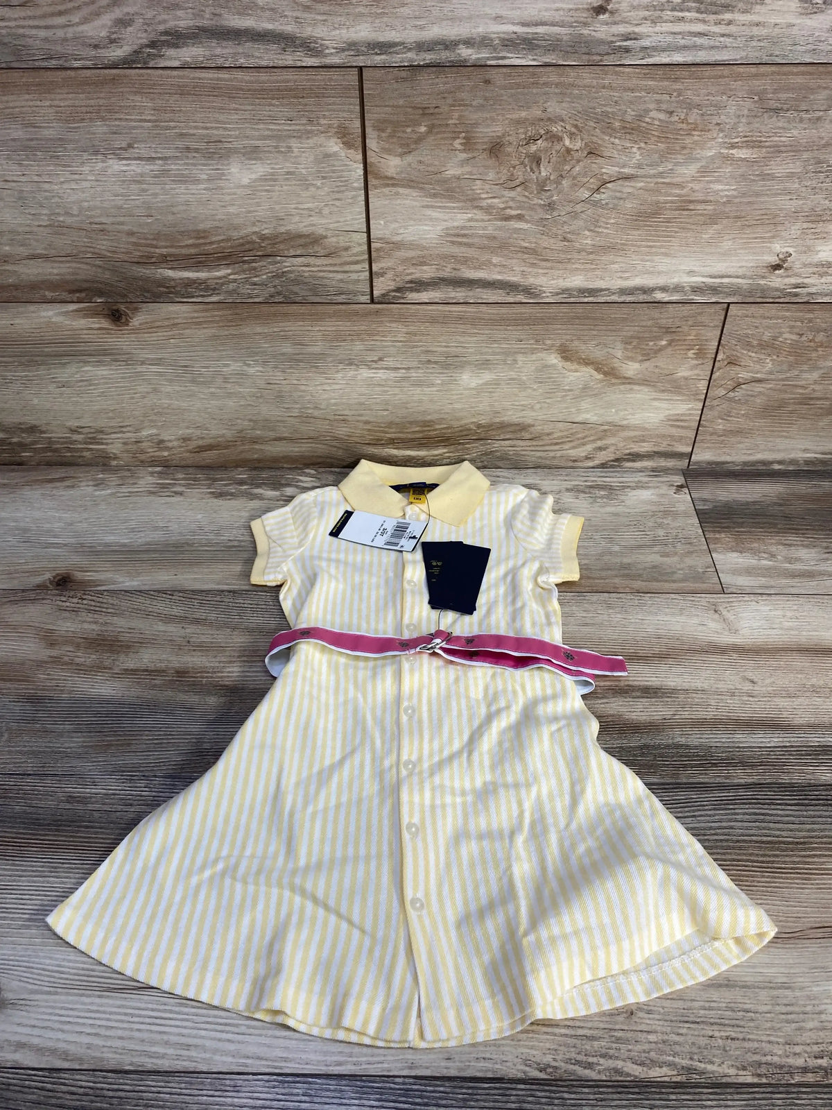 Flat lay of Polo Ralph Lauren girls belted knit oxford polo dress, size 3T, yellow and white stripes with pink belt on wood floor