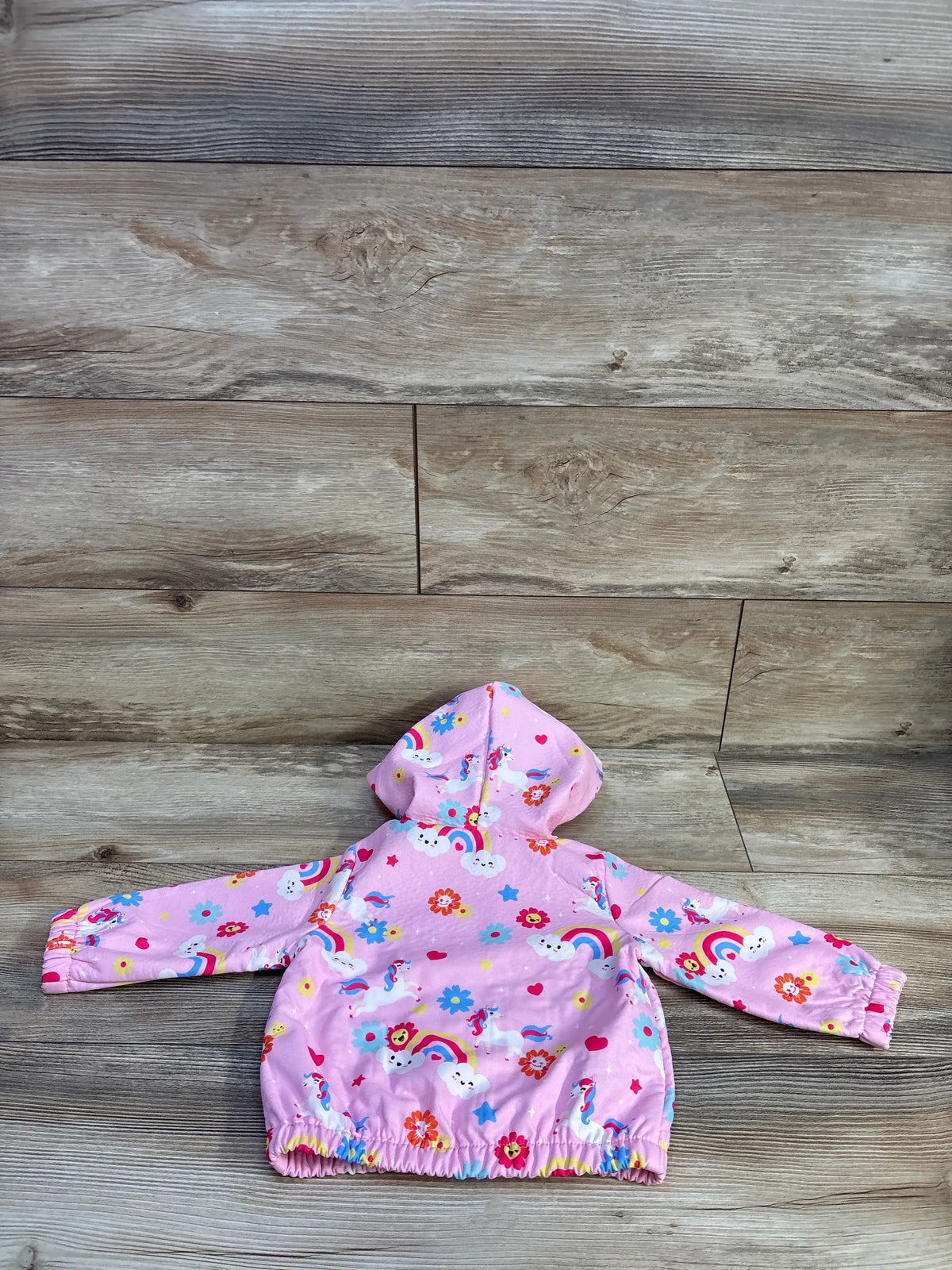 Back view of pink toddler hooded jacket showcasing unicorn, rainbow, cloud, and flower print with elastic hem and cuffs on wooden floor background