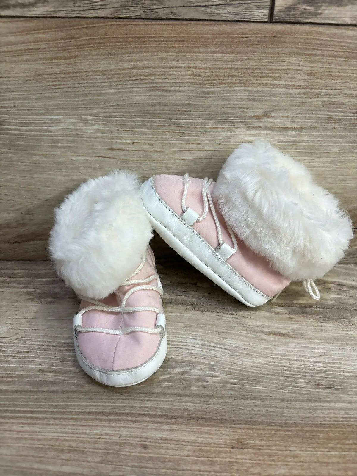 Pink baby shoes with white fur trim and white soles on wooden background