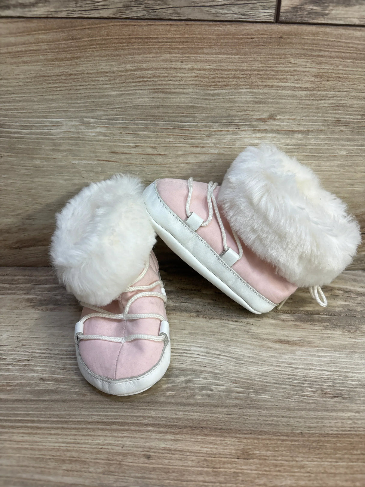 Pink baby shoes with white fur trim and white soles on wooden background