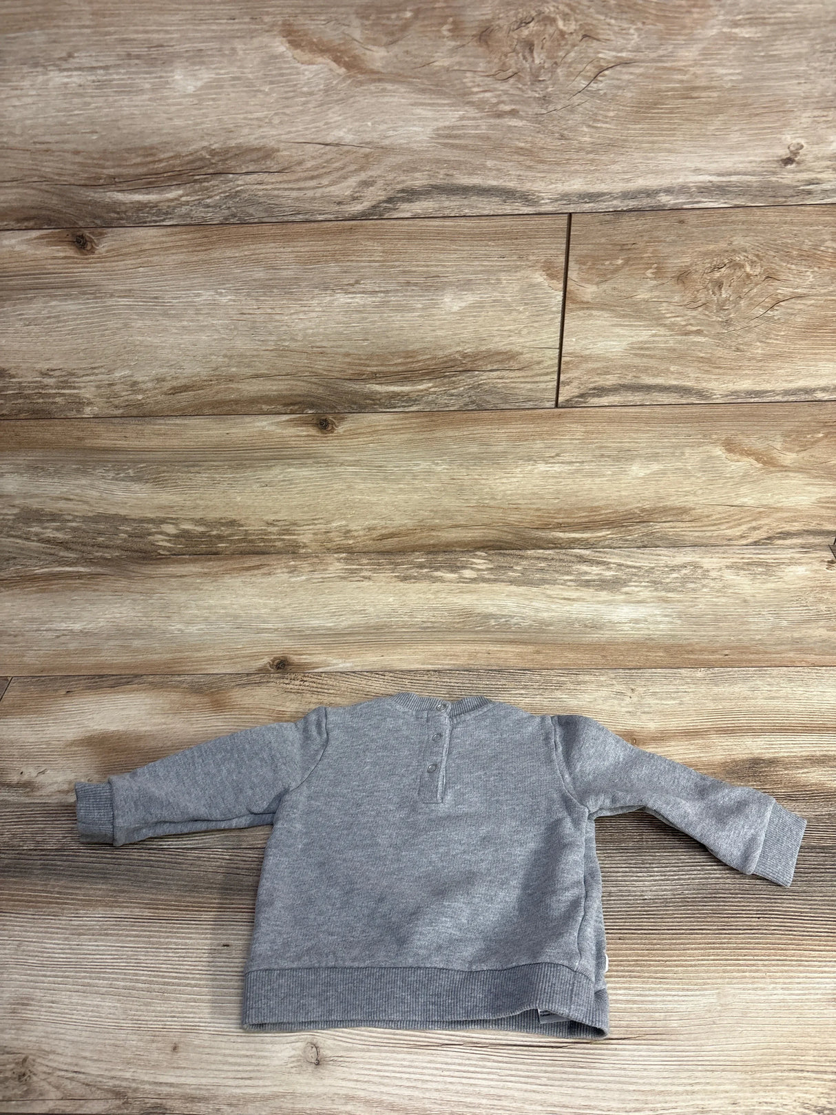 Back view of a gray long-sleeve toddler sweatshirt on wooden floor