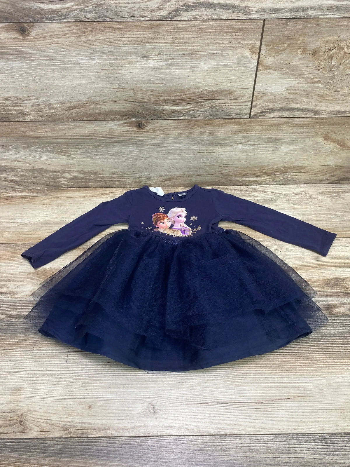 Flat lay of navy H and M Frozen tulle dress for toddler, showing layered skirt and character-print bodice on wood background