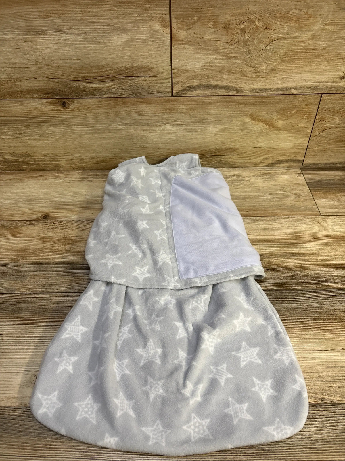 Top-down view of Halo grey fleece sleepsack swaddle showcasing white star print and swaddle wing with wood background