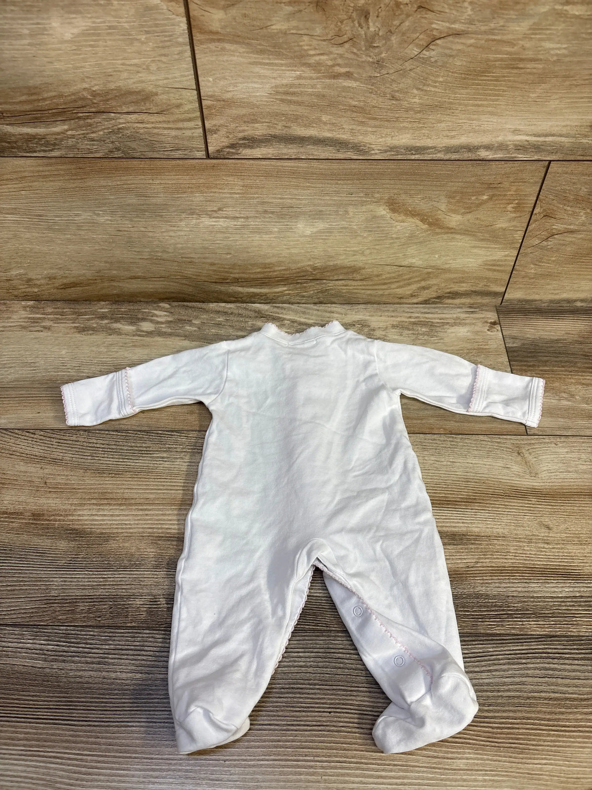 Overhead view of white Kissy Kissy snap sleeper in newborn size showcasing long sleeves and footed legs on wood floor