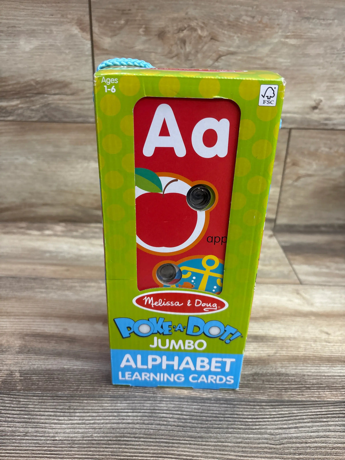 Front view of Melissa and Doug Poke a Dot Alphabet Jumbo Learning Cards showing an Aa apple card on a wood floor
