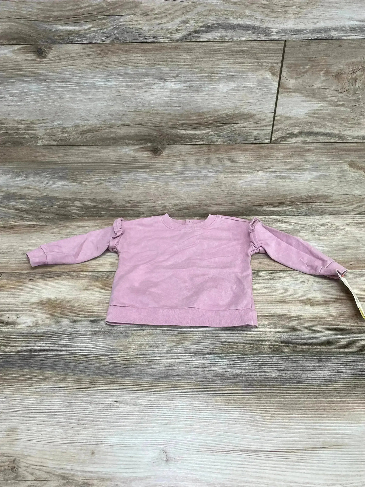 Flat lay of pink Cat & Jack baby sweatshirt size 6-9 months showing ruffle shoulder detail on light wood background