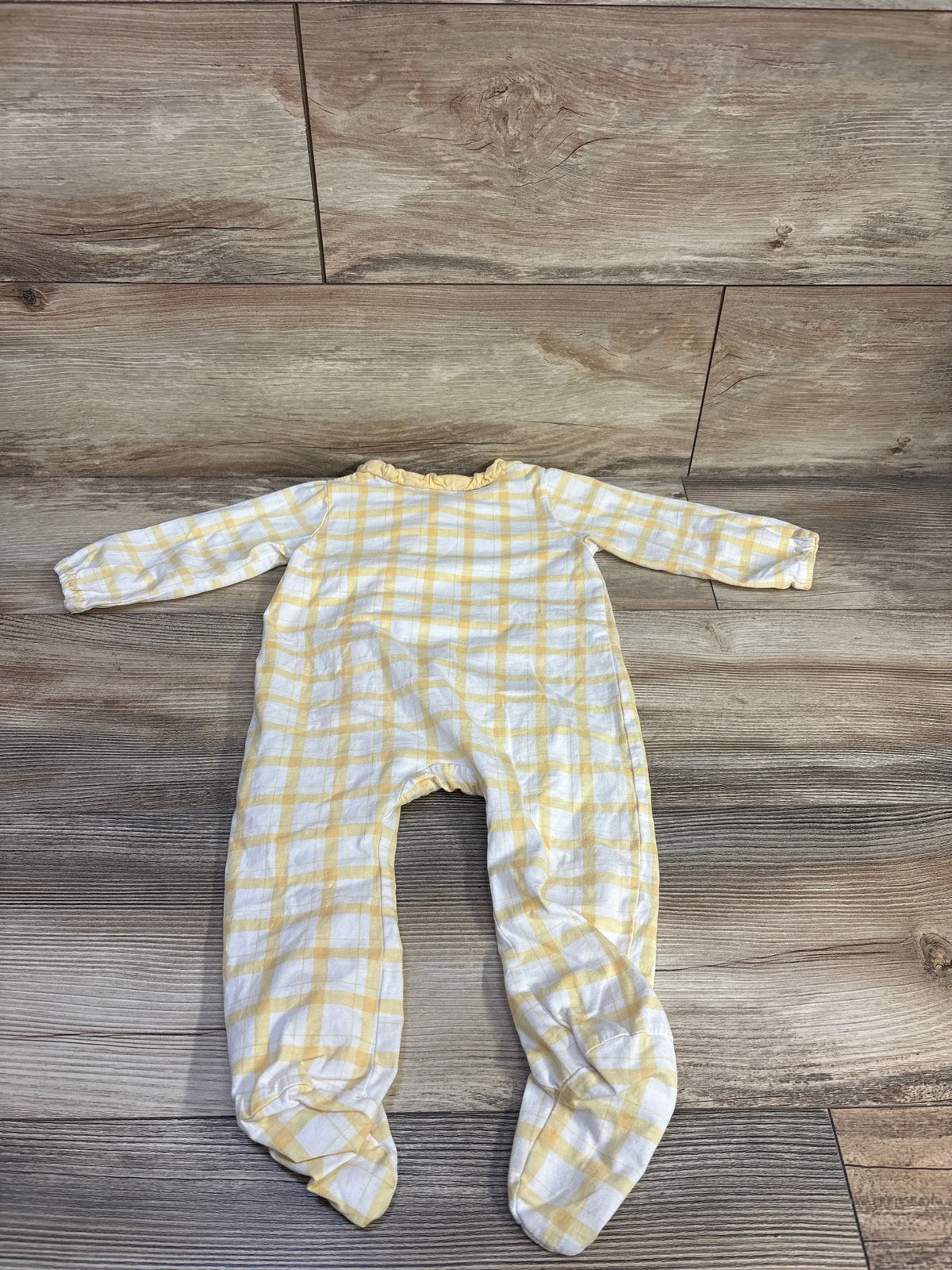 Front view of yellow side snap ruffle sleeper with long sleeves and plaid pattern on a wood-look background