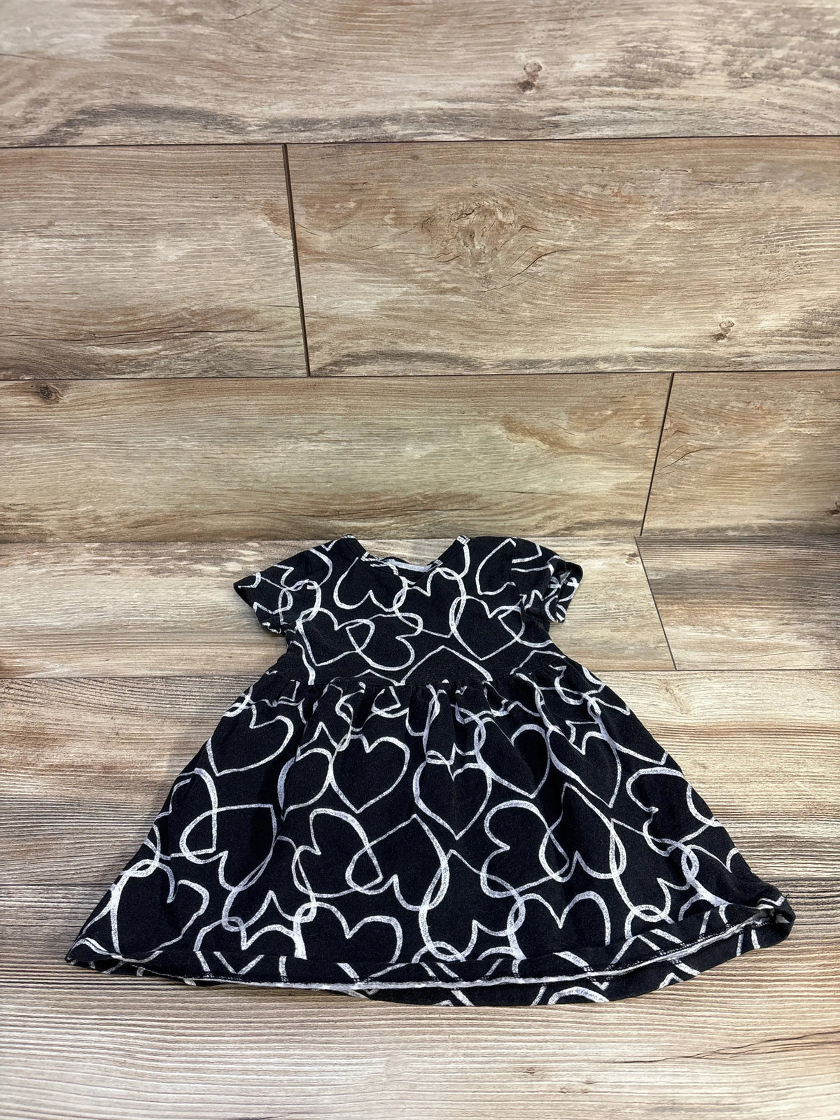 Flat lay of Jumping Beans toddler dress, black with white heart print, short sleeves and gathered skirt on wood background