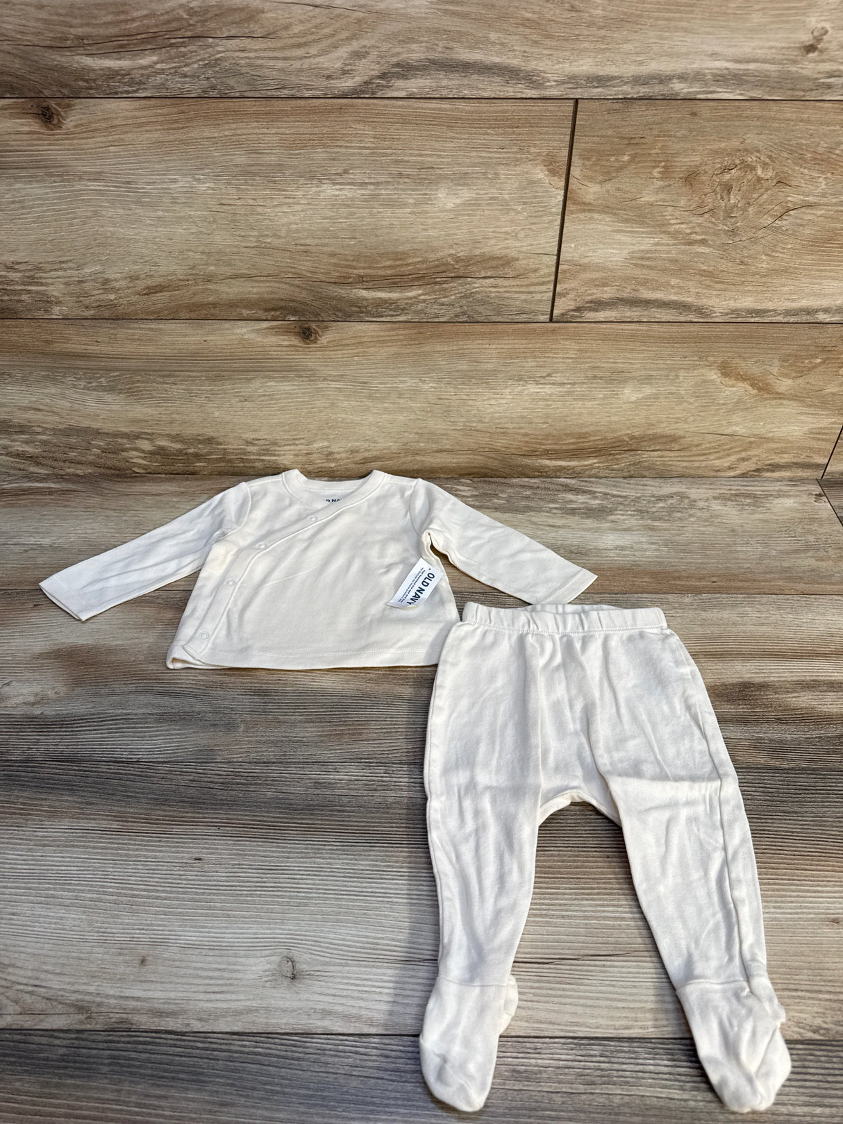 Cream-colored baby kimono top and footed pants laid on wooden floor background