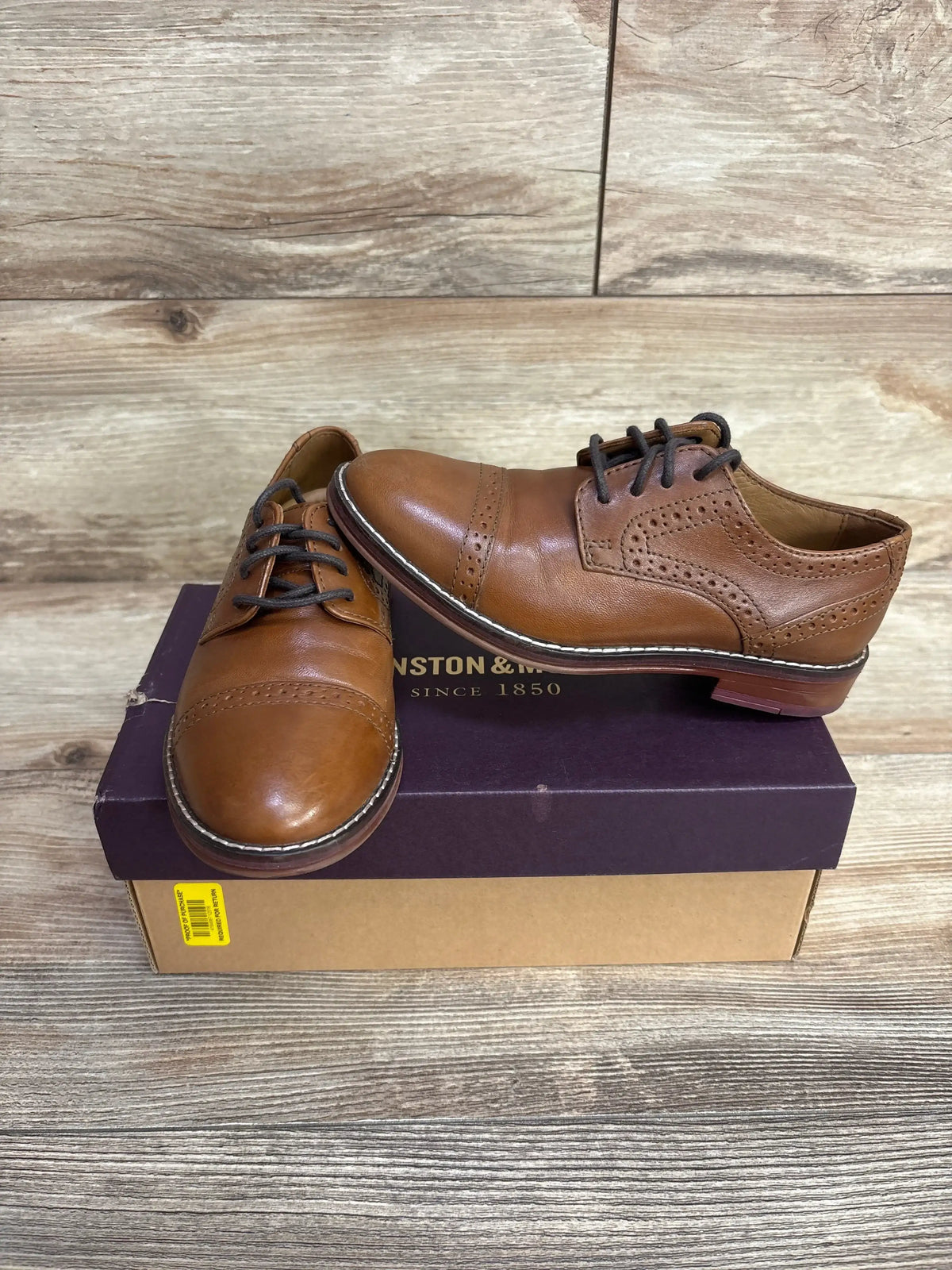 Three-quarter view of Johnston & Murphy cap-toe brown leather shoes size 12C showing perforated brogue detail on purple box