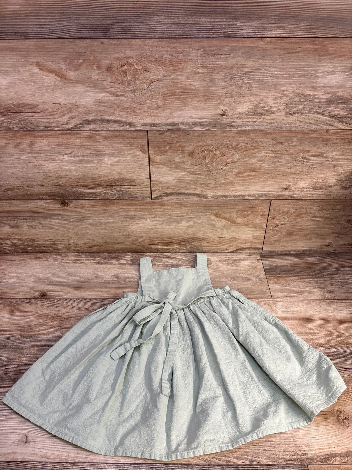 Front view of green sleeveless button-front dress in size 2T showcasing gathered skirt and waist tie on wood planks