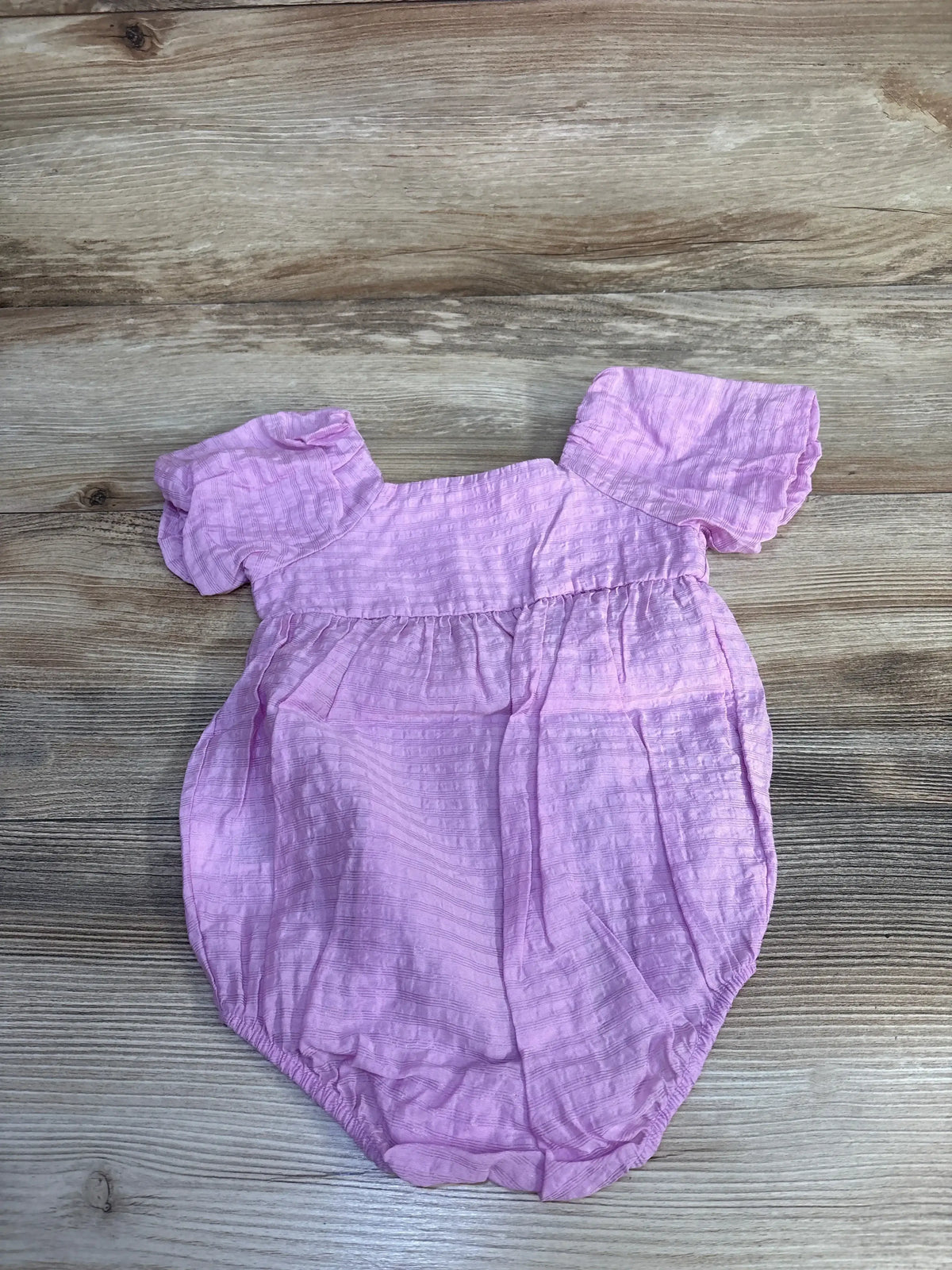 Flat lay of purple bubble romper with puff sleeves, square neckline and elastic leg openings on wood background