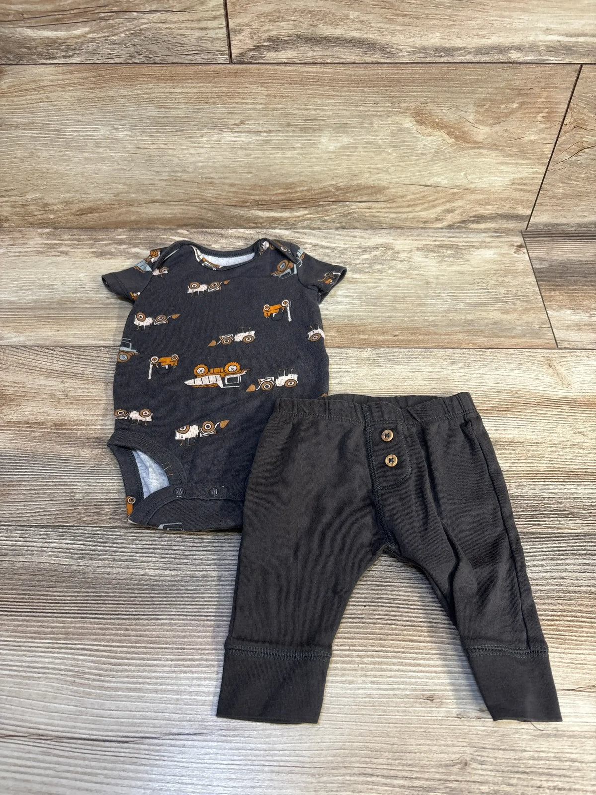 Baby boy outfit with dark tractor print onesie and black pants on wood floor