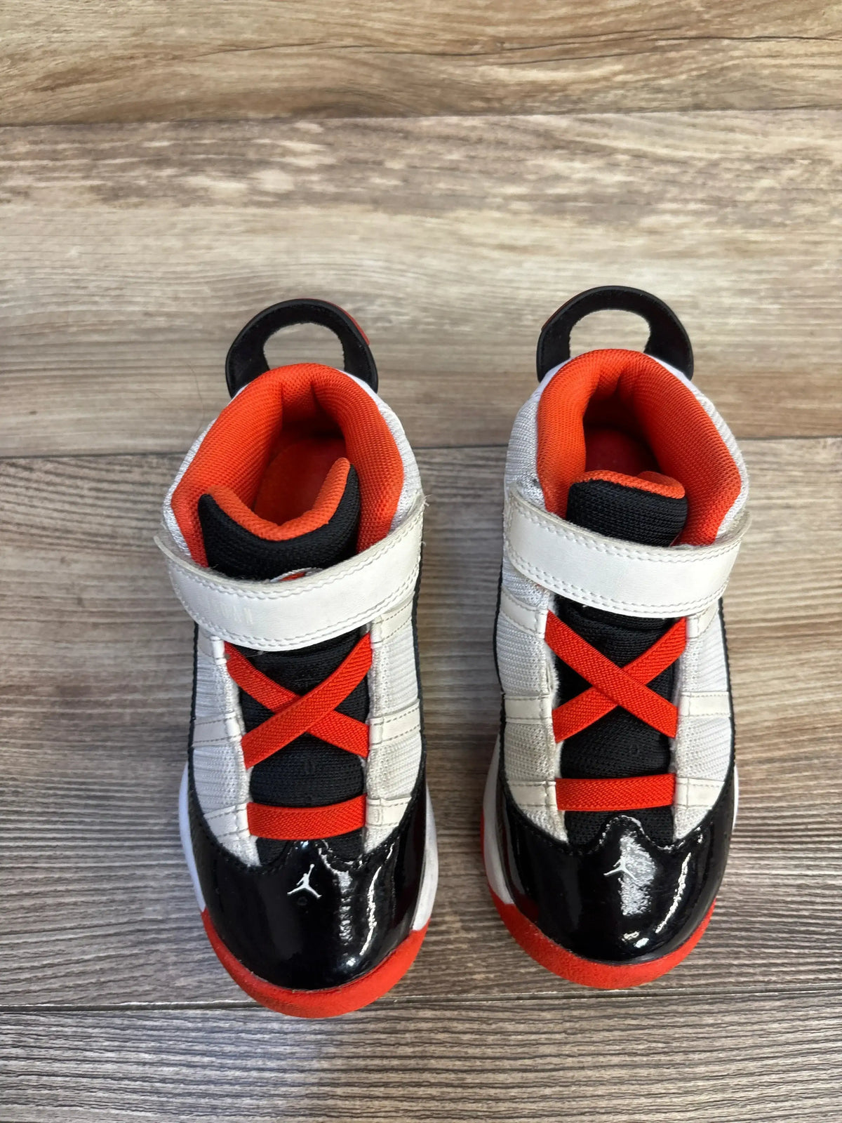 Top view of Air Jordan 6 Rings TD sneakers with black patent toe, orange lining, velcro strap, and pull tab on wood floor