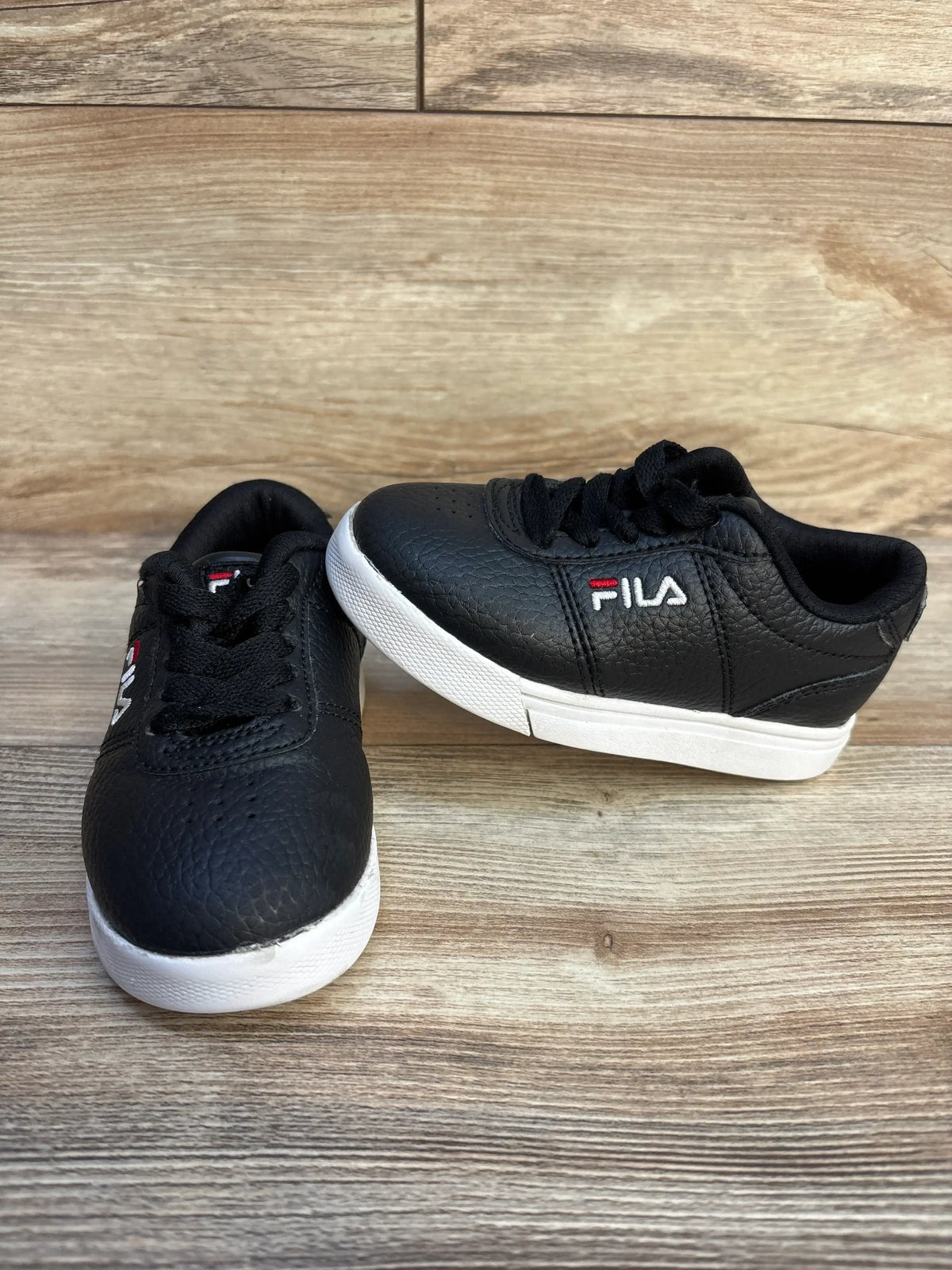 Pair of black Fila sneakers with white soles on wooden surface