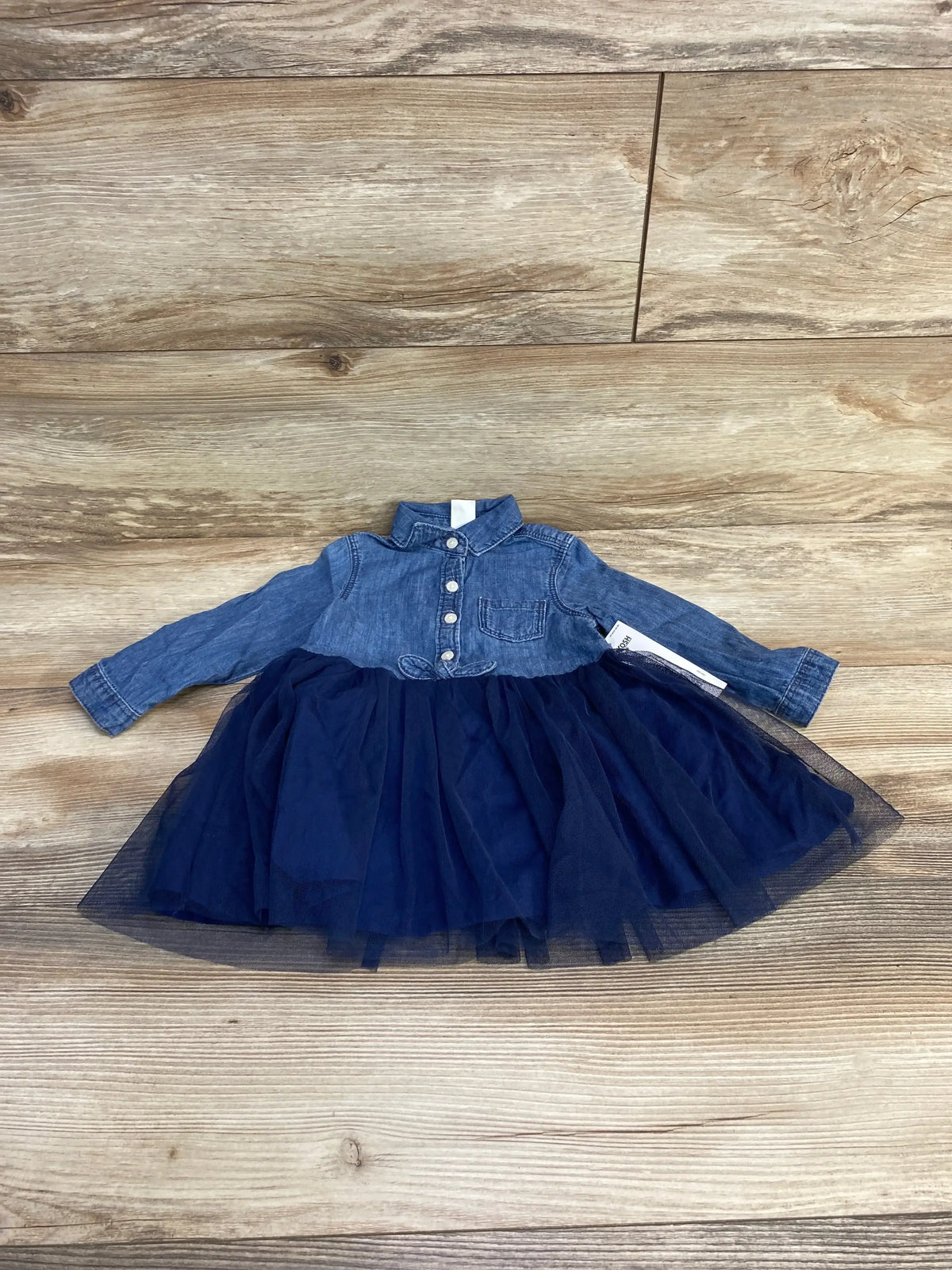 Flat lay of OshKosh chambray baby dress with navy tulle skirt showing button-front denim bodice and layered tulle on wood background