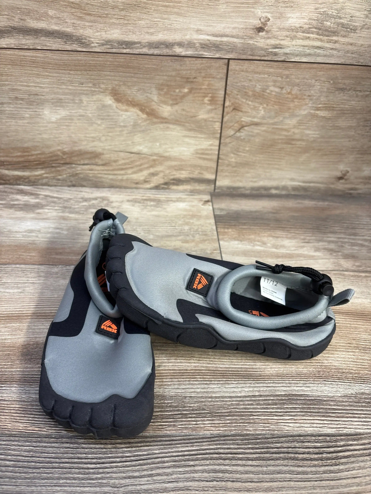 Three-quarter view of RBX grey kids water shoes with five-toe rubber soles and heel bungee, wood background, size 11/12C