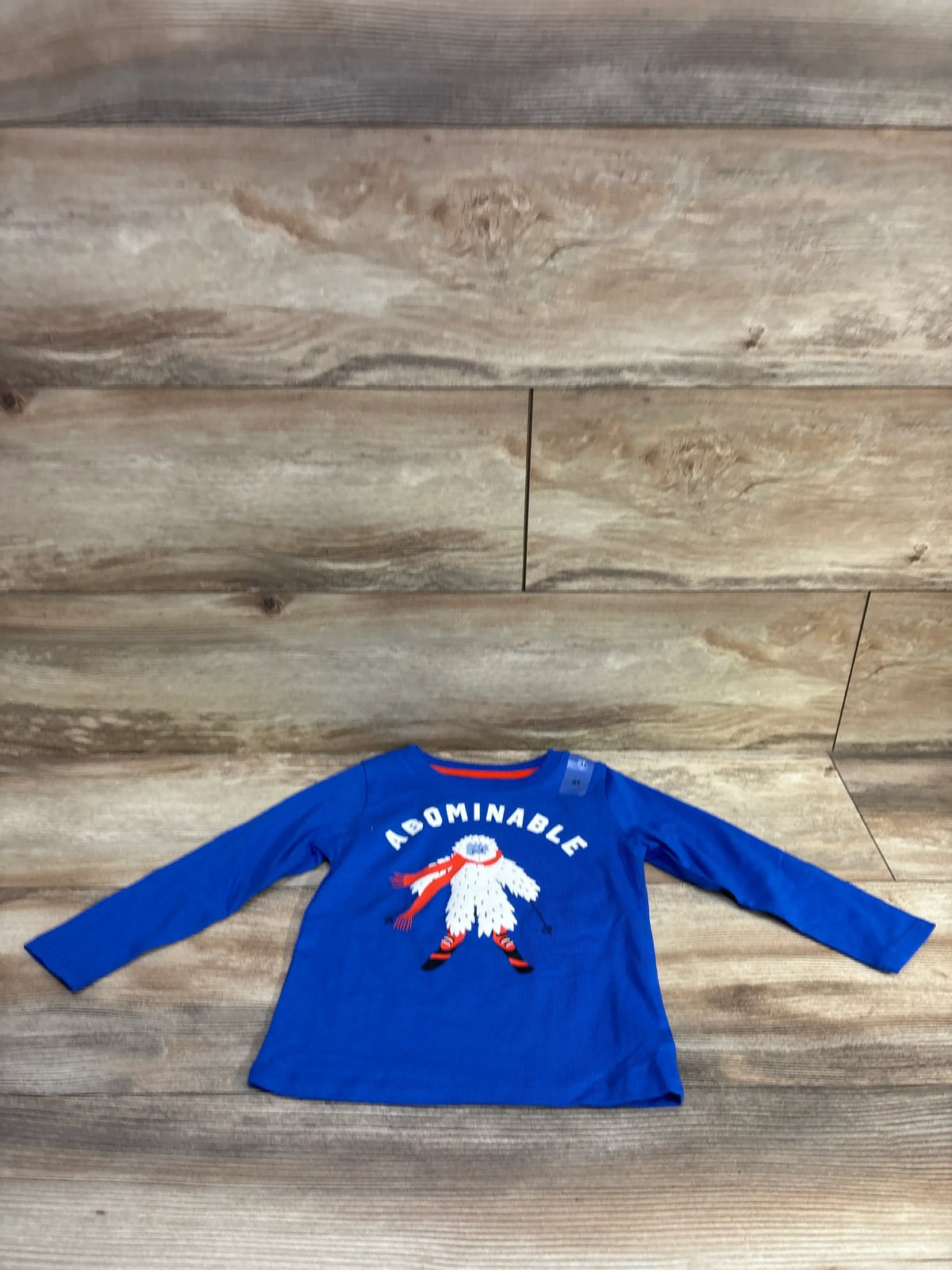 Flat lay of Epic Threads blue long sleeve toddler shirt with white yeti graphic and ABOMINABLE text on wood background
