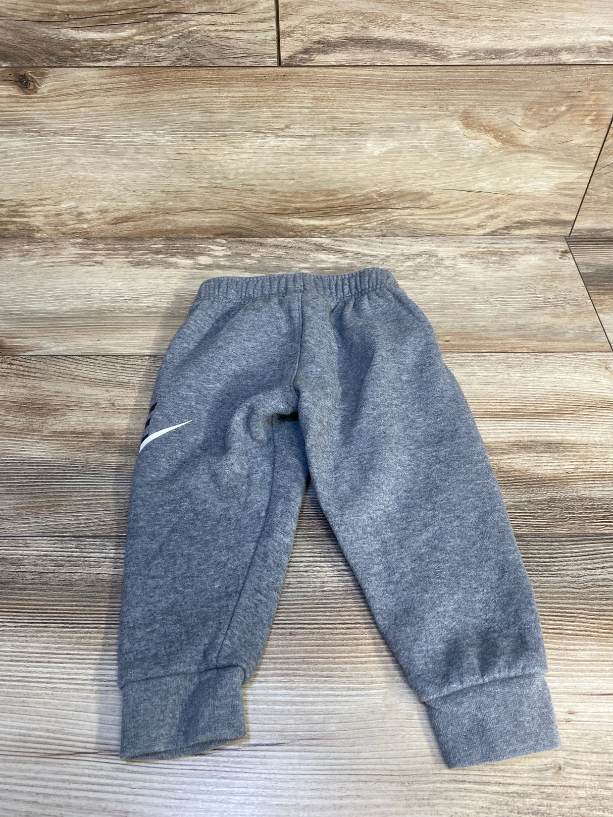 Gray kids sweatpants with elastic waistband and cuffed ankles on wooden floor
