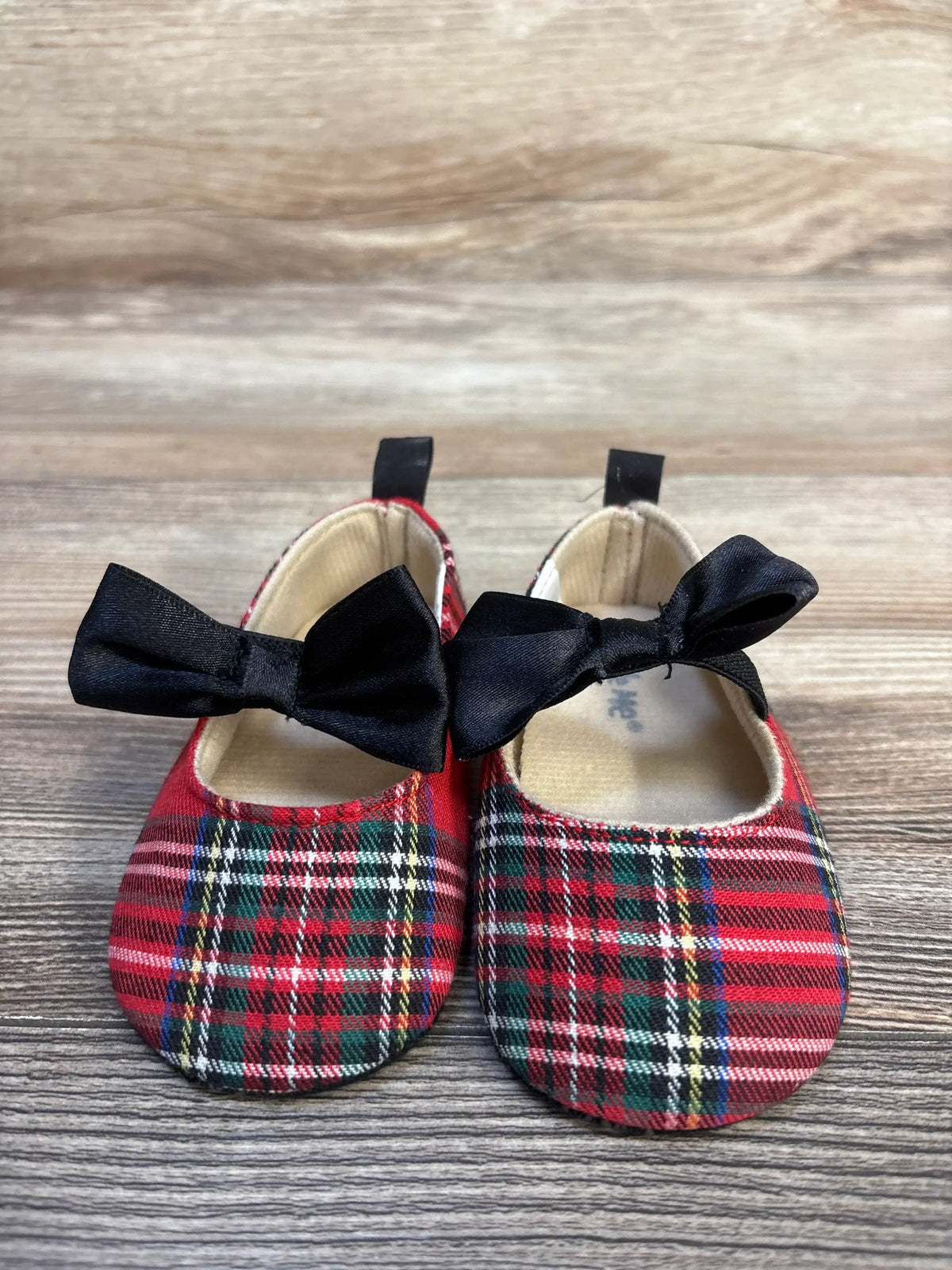 Red plaid baby shoes with black bows, soft sole, on wood background