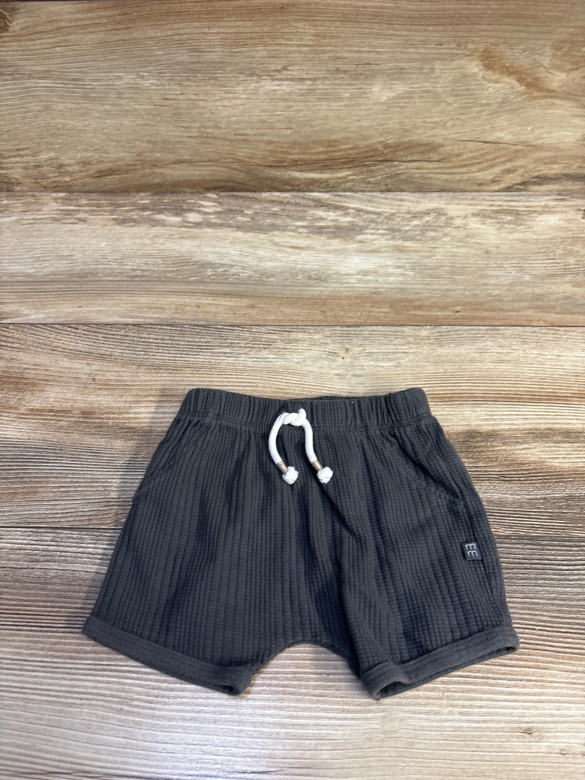 Front view of toddler drawstring shorts, size 12 months, showing white drawstring, ribbed grey fabric on wood background