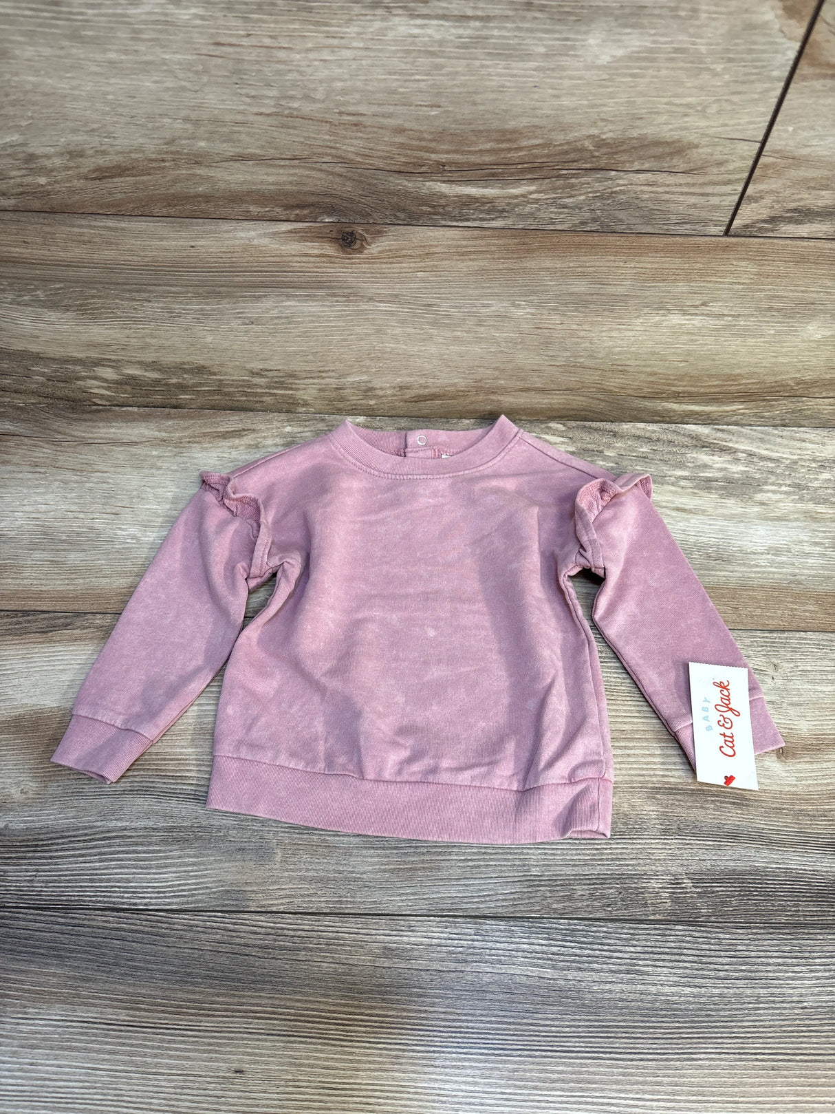 Pink long sleeve toddler sweatshirt with ruffle shoulders, Cat & Jack tag, on wood background