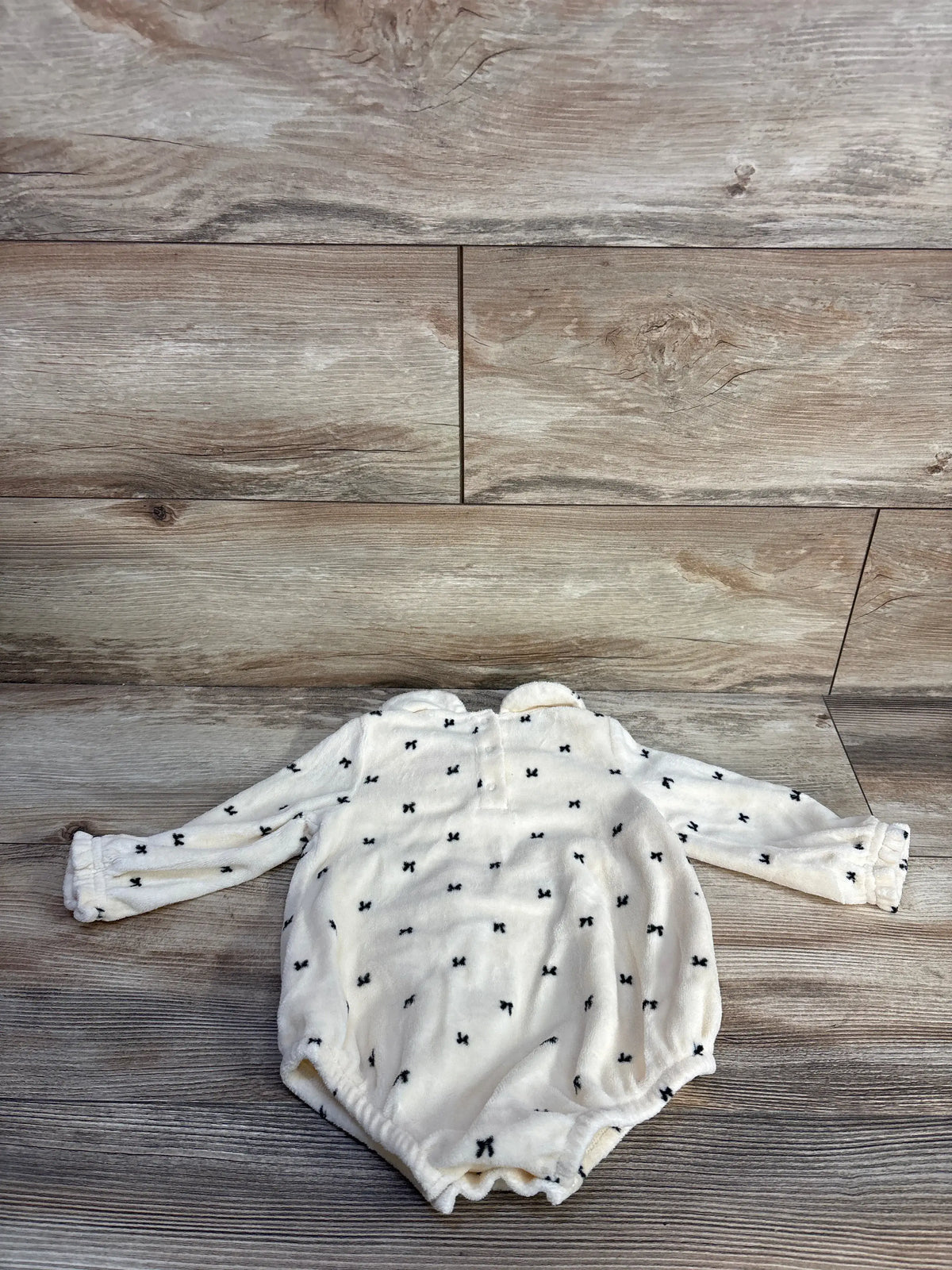 Front view of Cat & Jack ivory collared long sleeve bubble romper with black bow print on a wood floor