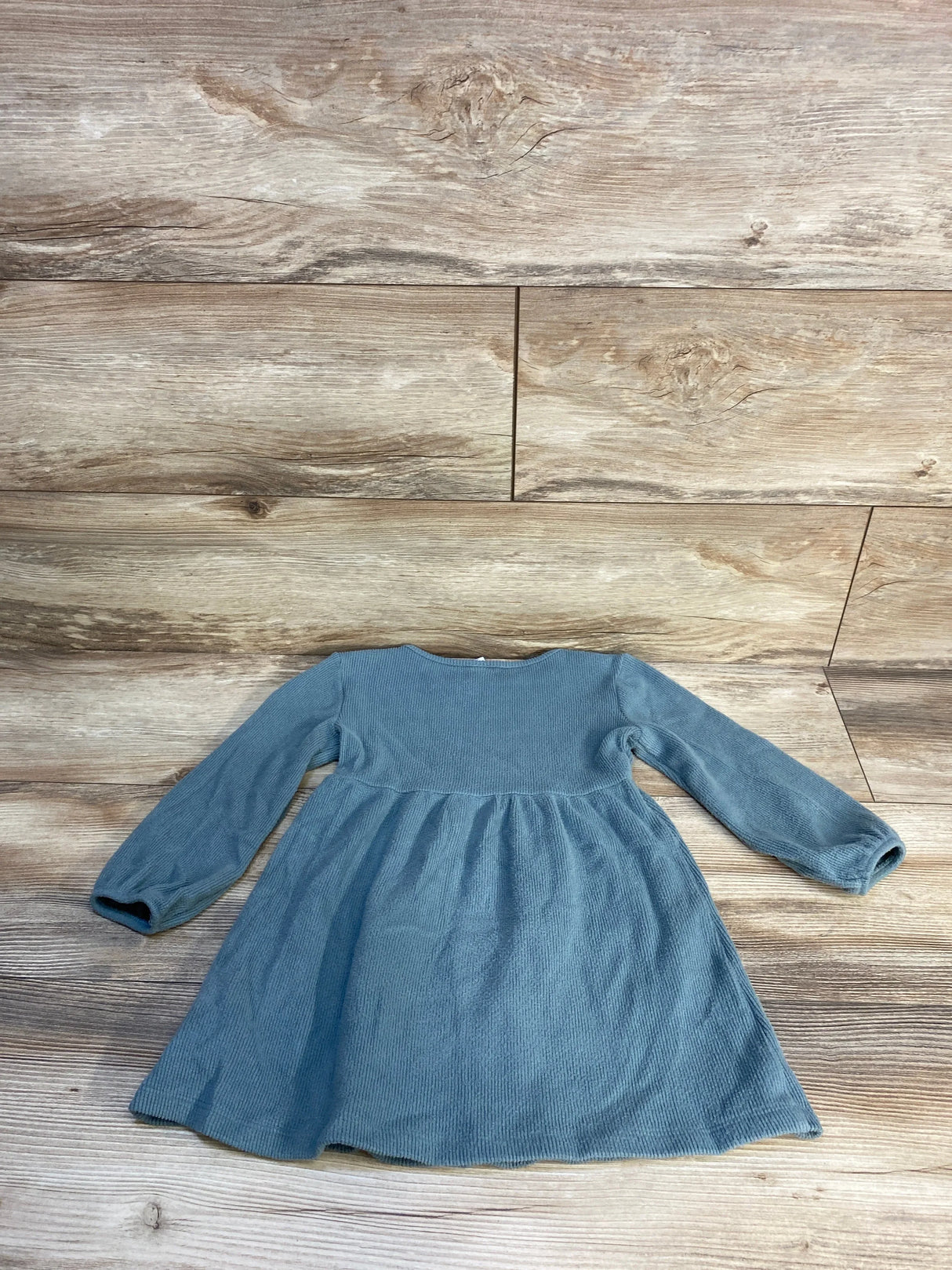 Blue long sleeve toddler dress laid flat on wood floor