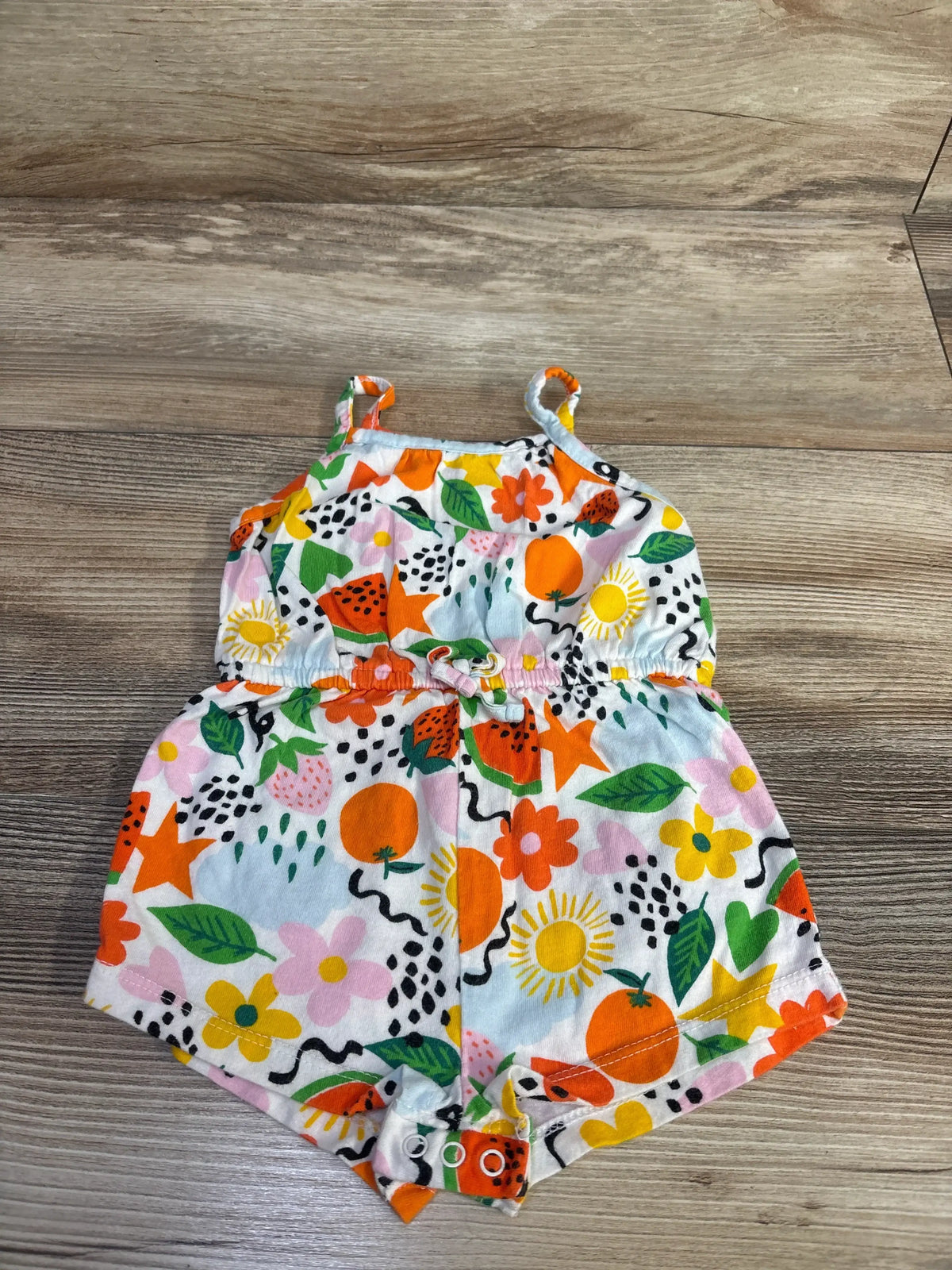 Flat-lay of Baby Gap sleeveless jersey-knit romper showing mixed fruit print, elastic waist, and snap closures at crotch on wood background