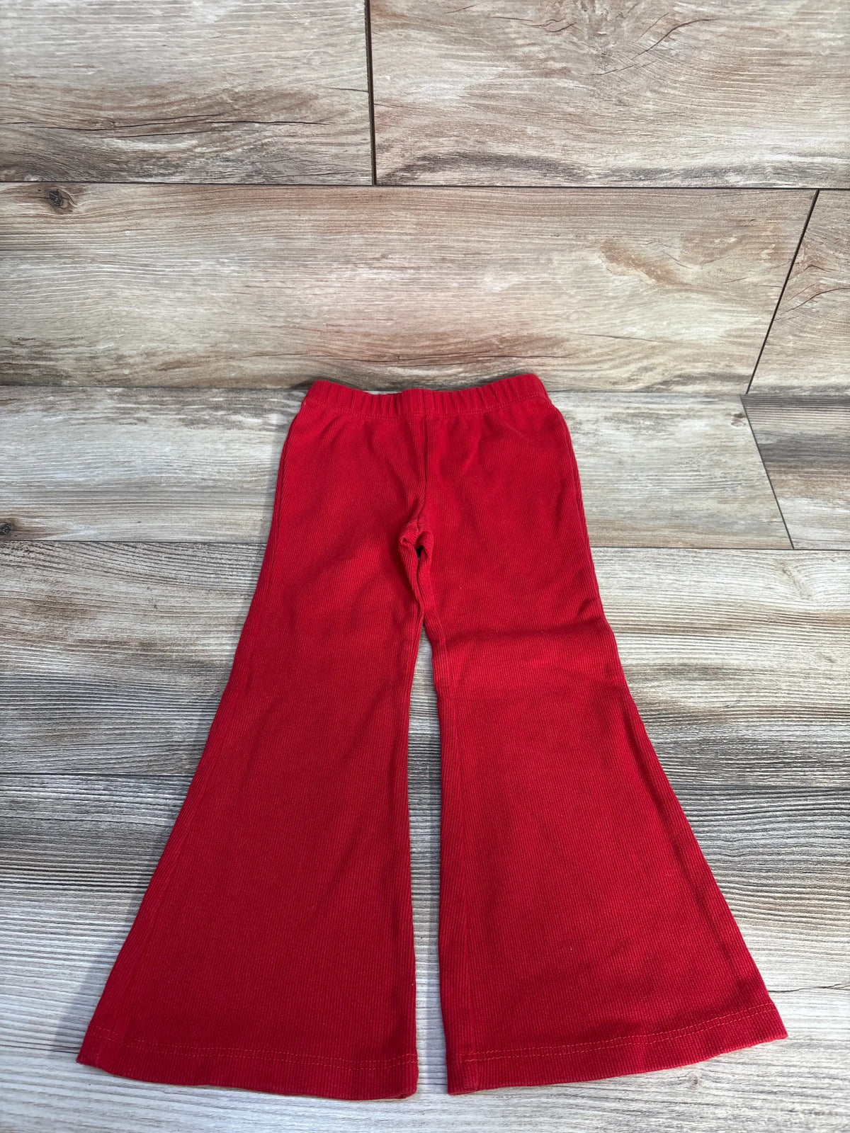 Front view of Baby Gap ribbed flare leggings showcasing red ribbed fabric and flared legs on a wood-look background