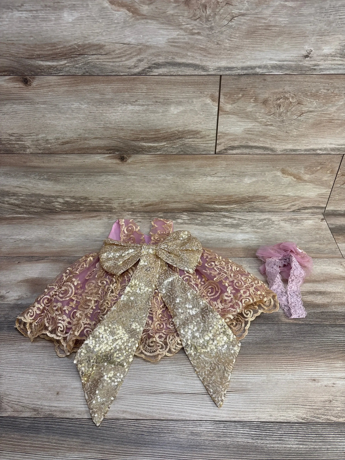 Flat lay of Melody dress set: pink tulle skirt with gold lace overlay, gold sequin bow and matching lace headband on wood