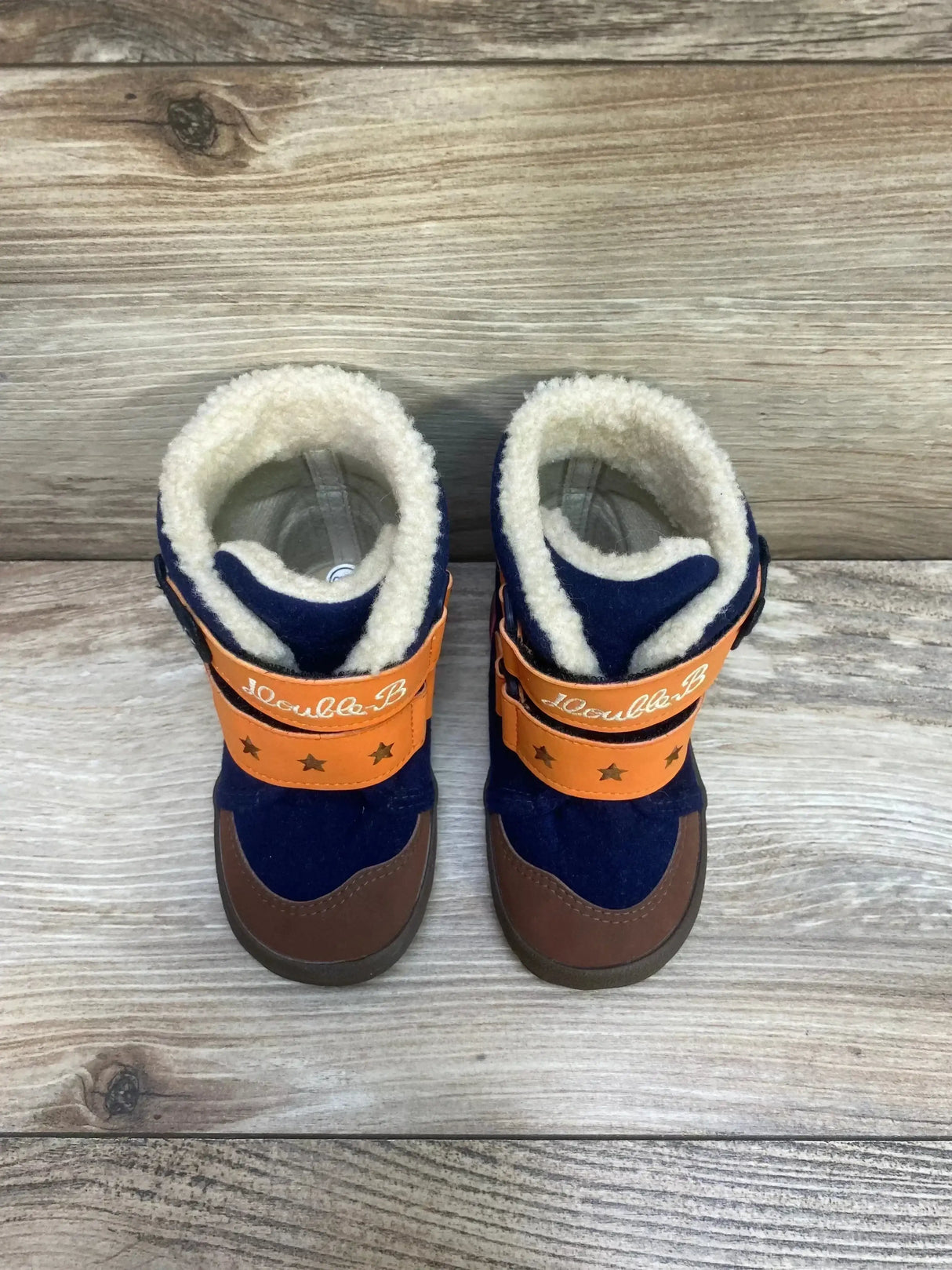 Top view of size 6 toddler winter boots with navy upper, brown toe, orange star Velcro straps and fleece lining on wood