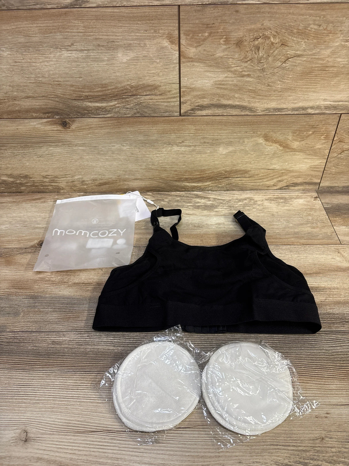 Top-down view of Momcozy pumping bra in black showing adjustable straps and removable nursing pads on wood background