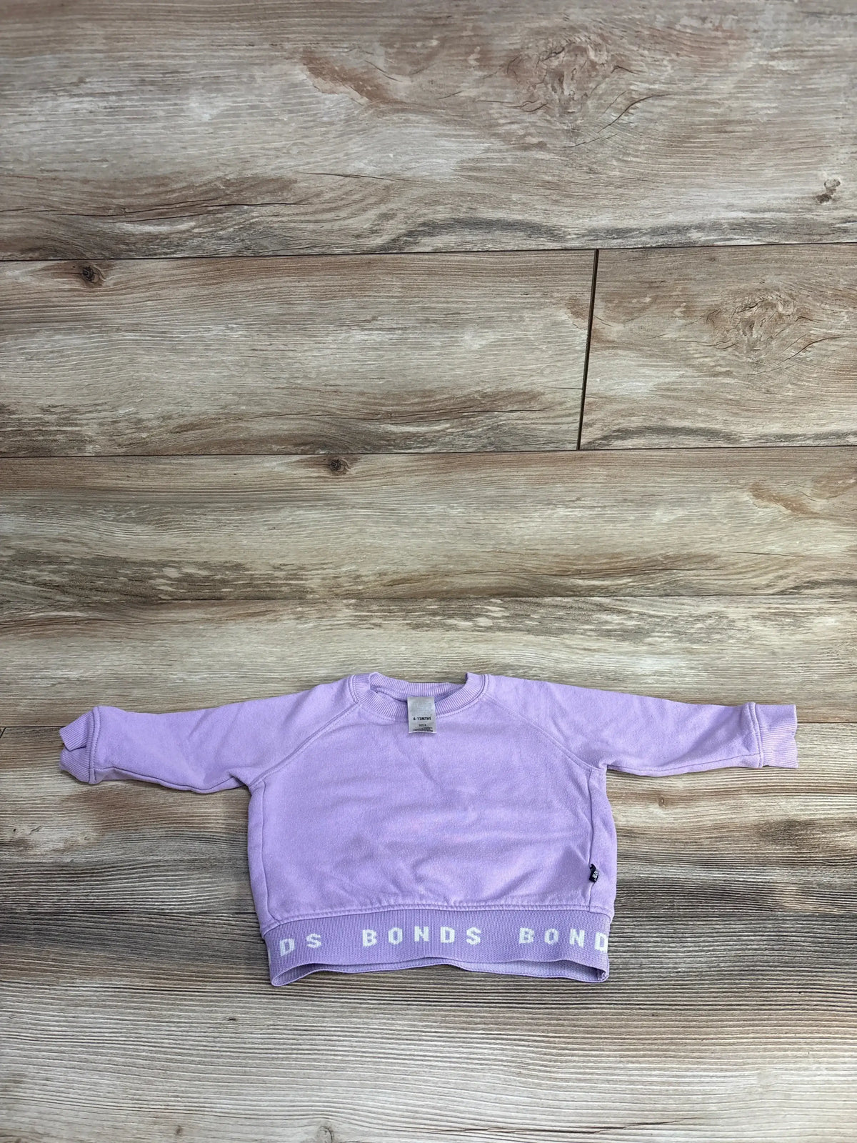 Lavender toddler sweatshirt with long sleeves and BONDS logo on hem on wooden floor