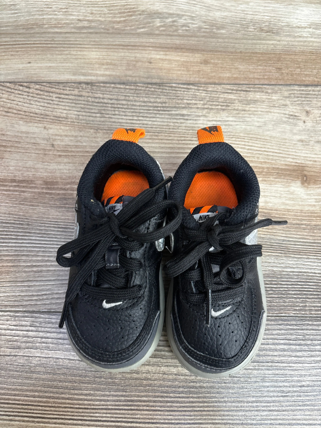 Top view of Nike Air Force 1 LV8 2 TD toddler sneakers sz 5C showing black leather uppers, orange lining, white Swoosh on wood background
