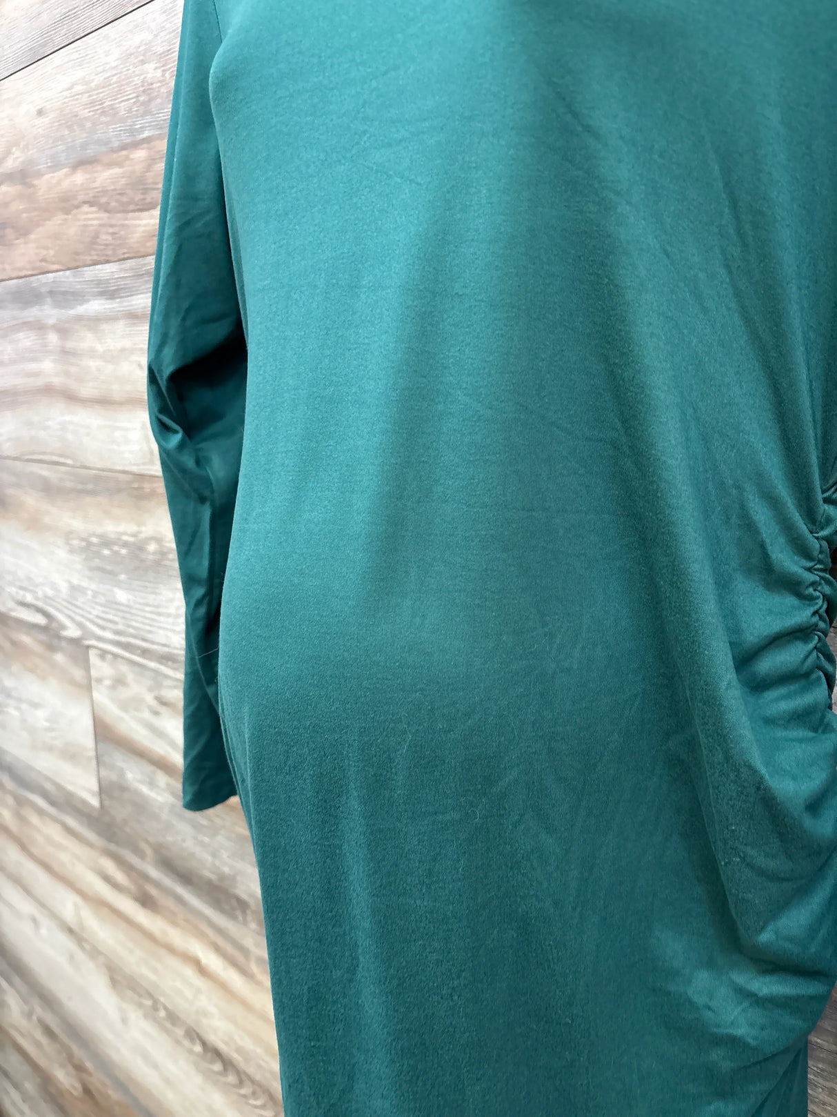 Side view of green long-sleeve maternity dress with ruched detailing against wood panel background