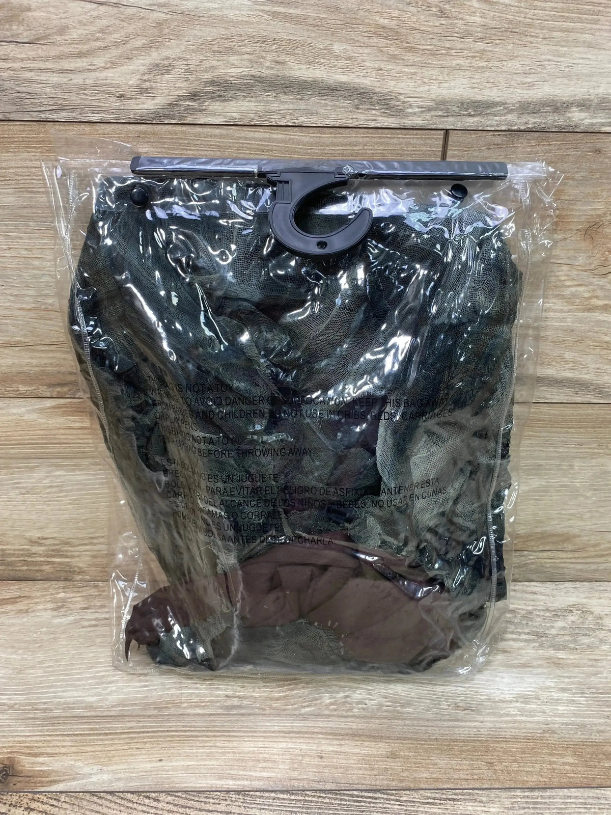 Front view of a shredded corpse costume in black and gray fabric inside a clear plastic package with a hanger on a wood floor