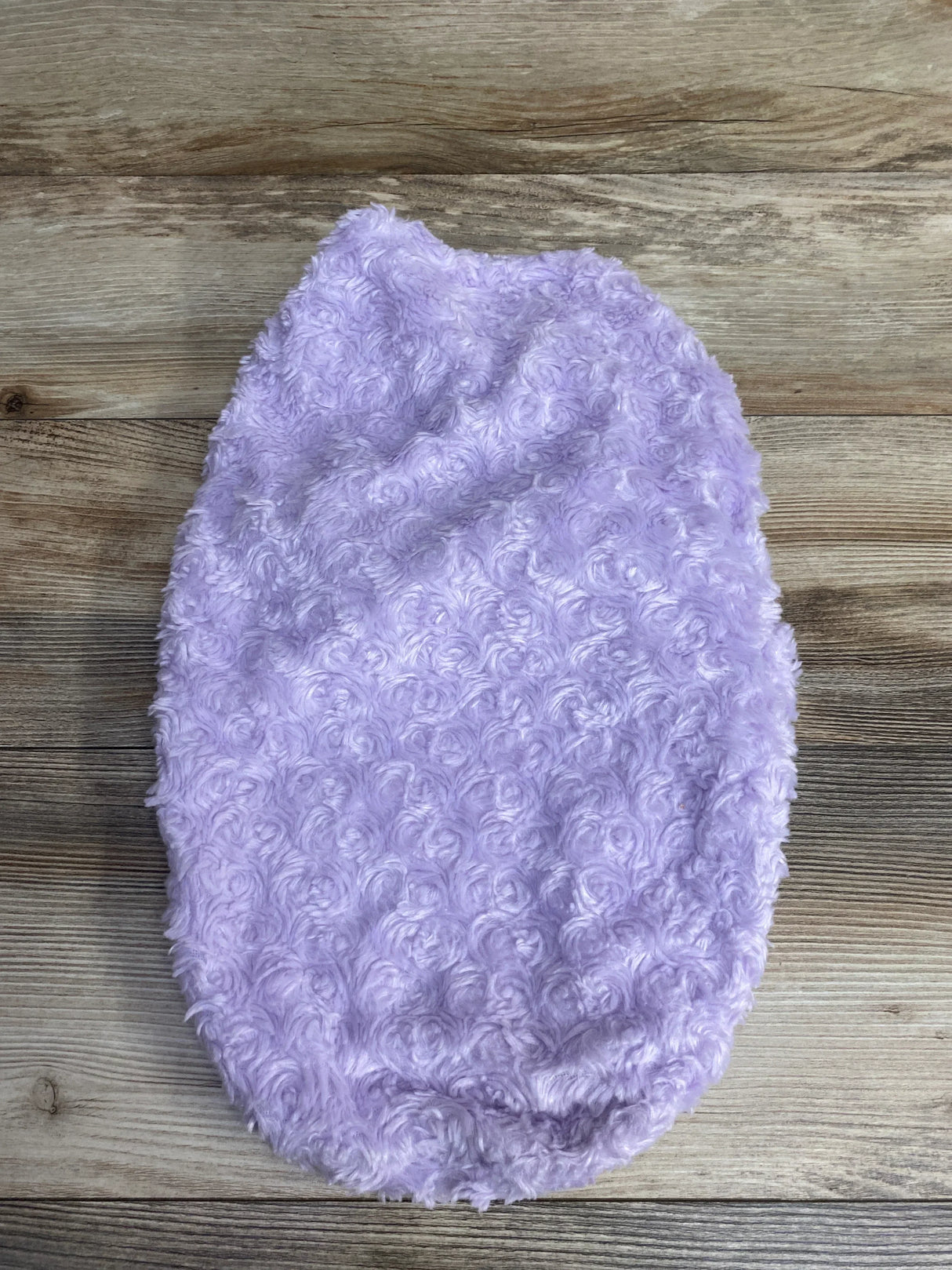 Soft lavender faux fur blanket with curly texture on wooden floor background