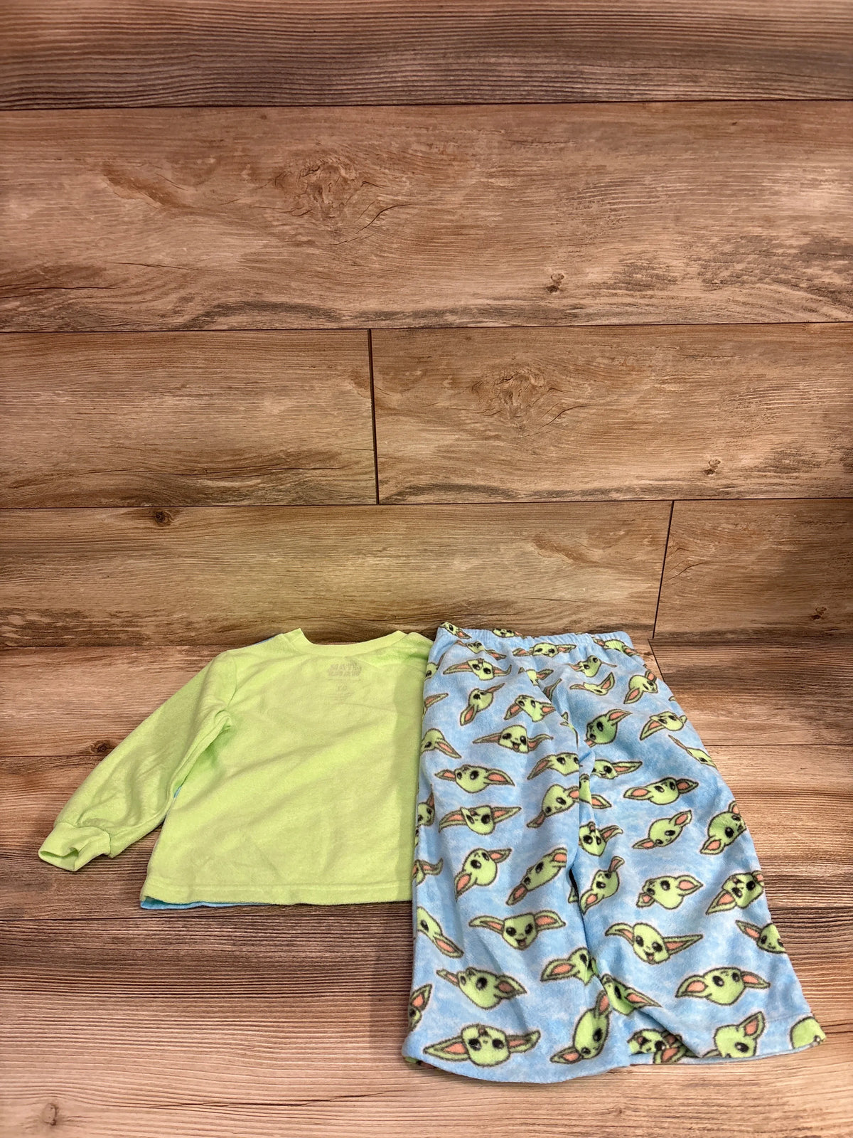 Two-piece Star Wars pajama set with lime green long-sleeve top and blue Grogu-print pants on a wood floor