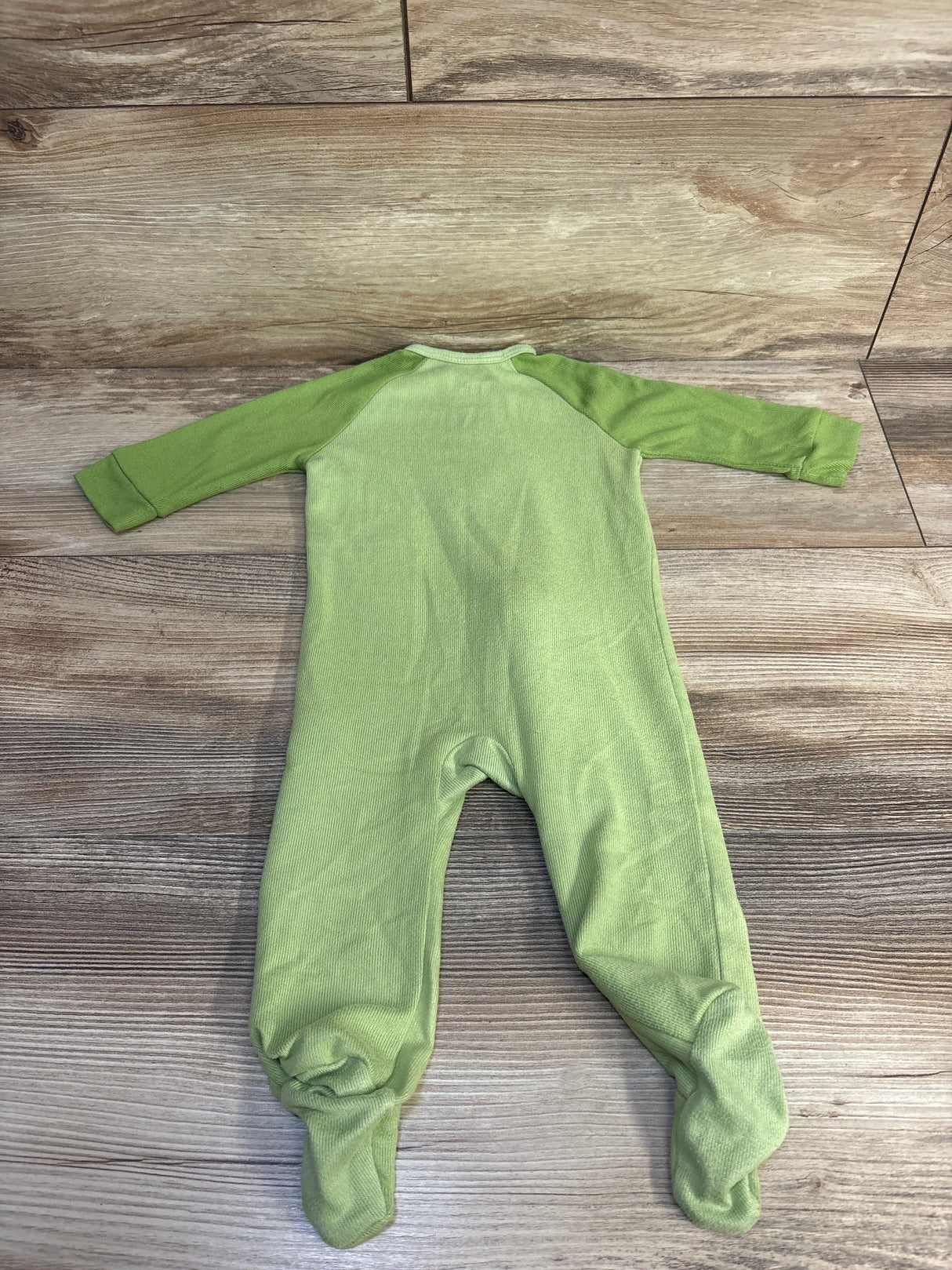 Back view of green Disney Baby The Lion King footed sleeper showing raglan long sleeves and built-in feet on wood floor background