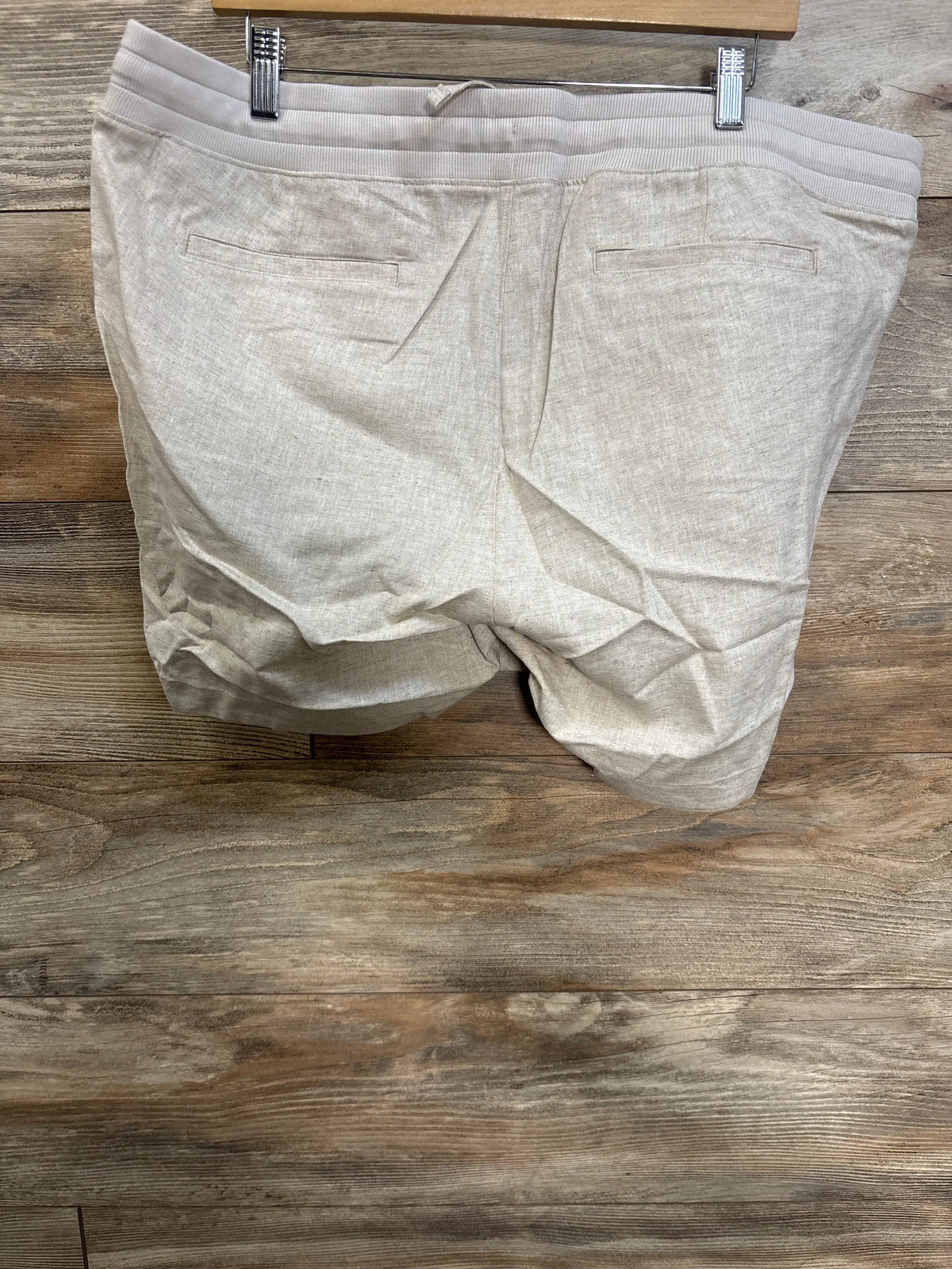 Back view of beige Gap maternity linen-blend shorts showcasing back welt pockets and elasticized under-belly waist on wood