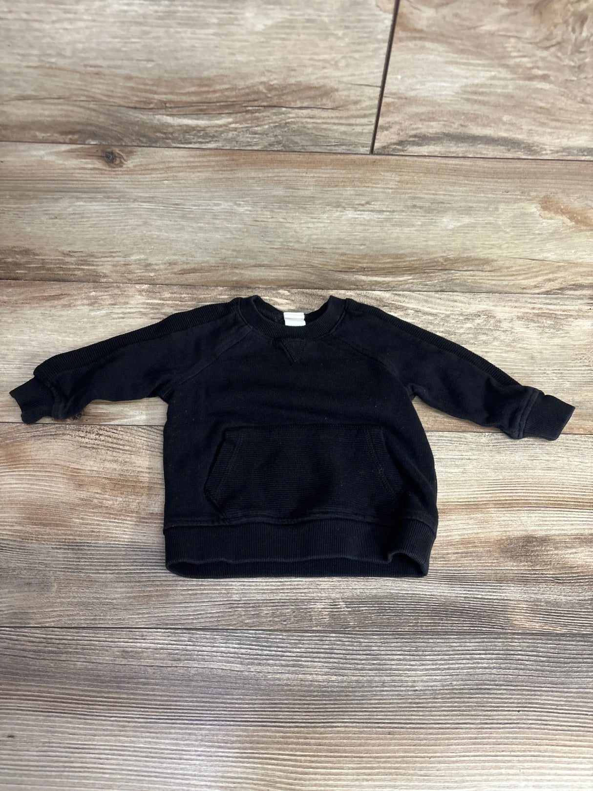Black toddler sweatshirt with long sleeves and front pocket on wood background
