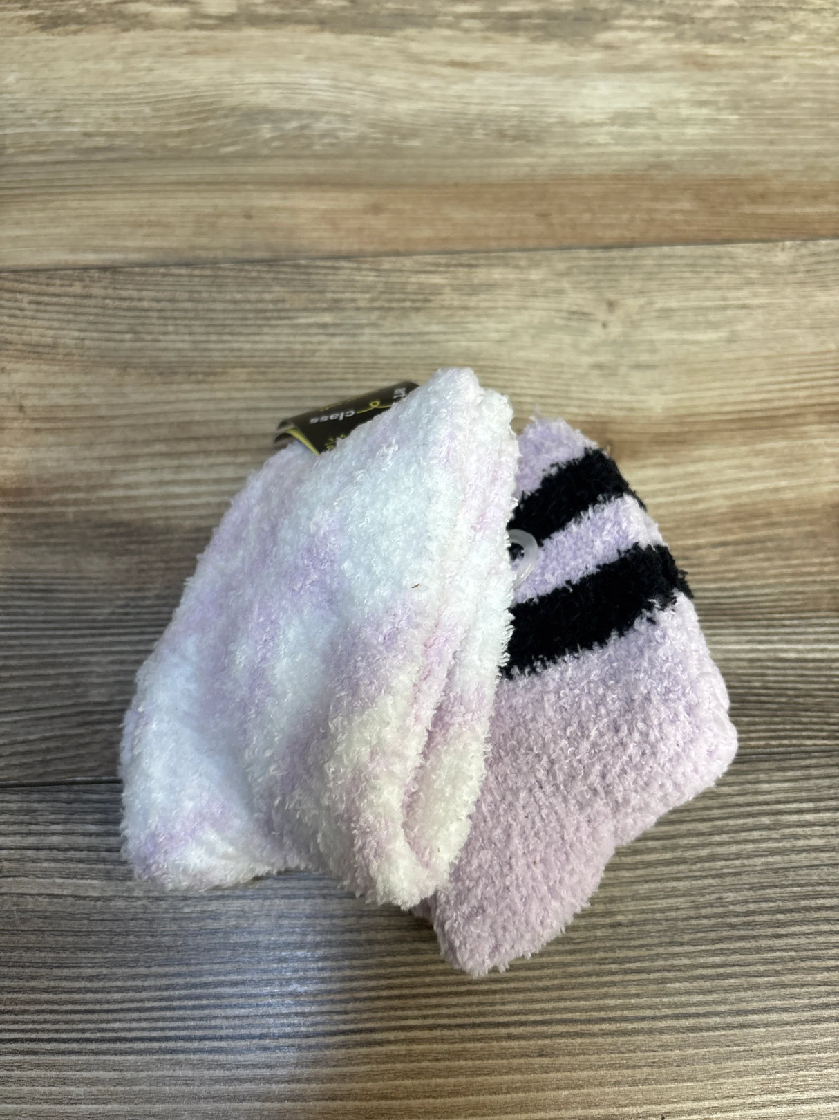 Soft pastel purple and white baby socks with black stripes on wood background