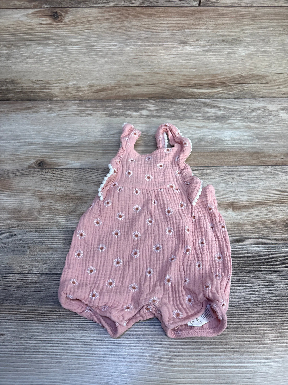 Top view of Emily & Oliver pink floral gauze romper for ages 3 to 6 months showcasing ruffled straps on a wood background
