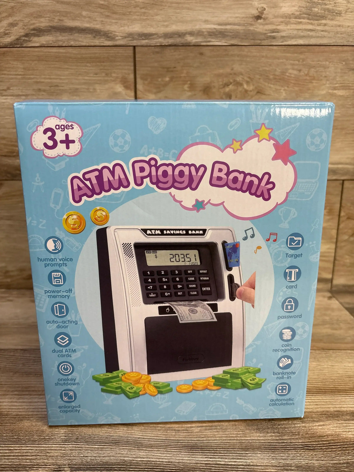 Front of Fishboy ATM Piggy Bank box showing toy ATM keypad, card slot, bill slot and play money on wood background