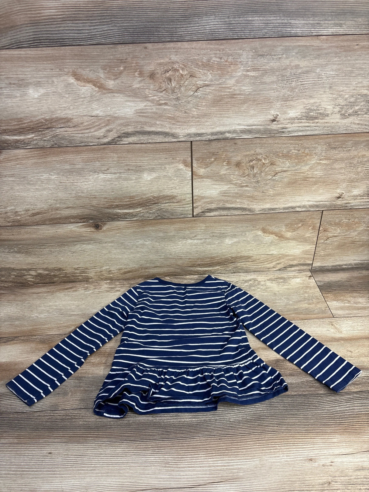 Front view of Carter's navy and white striped long-sleeve peplum top with ruffled hem on wood plank floor